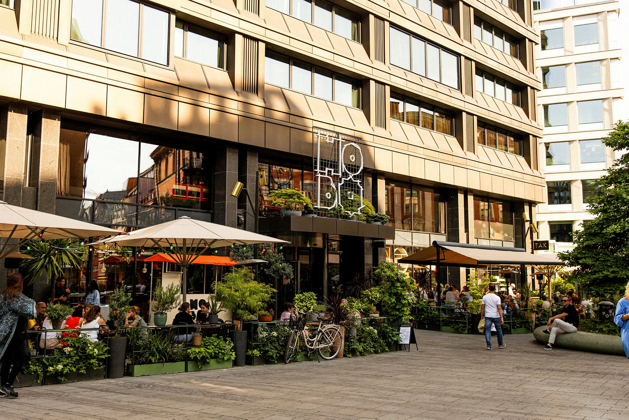 En uteservering foran en moderne bygning med store glassvinduer. (AI-generert tekst)