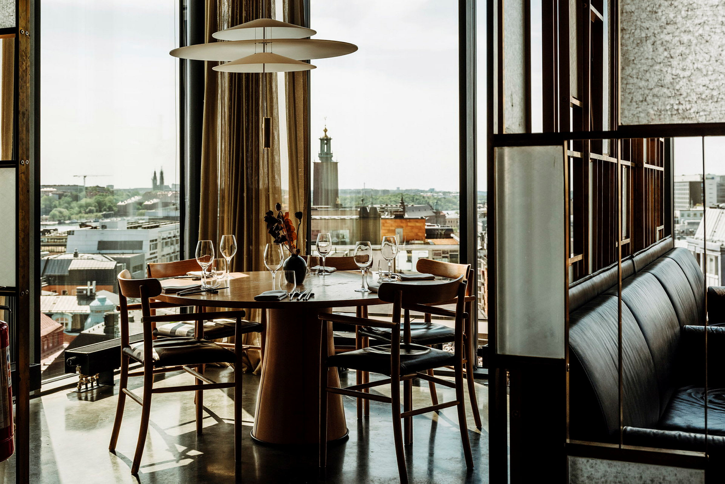 Et dekket bord for fire personer i en restaurant med utsikt over en by gjennom store vinduer. (AI-generert tekst)
