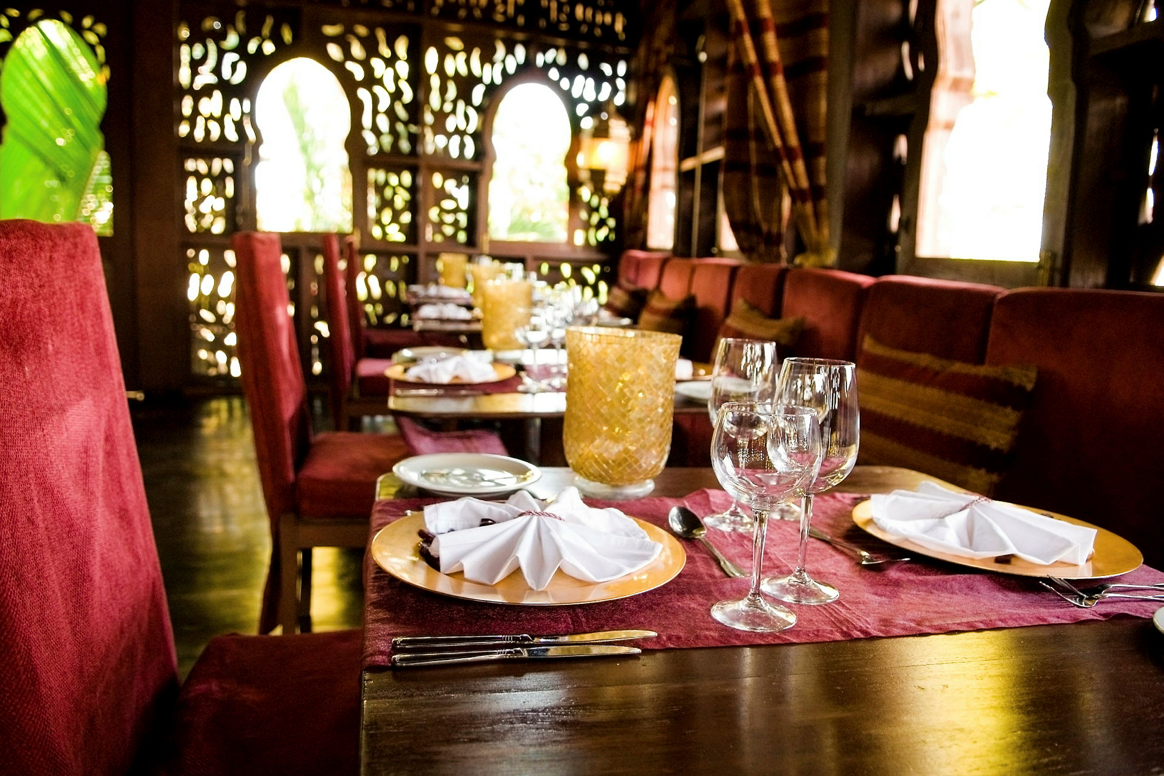 Et bord i en elegant restaurant med rødt interiør, dekket med tallerkener, glass og bestikk. (AI-generert tekst)