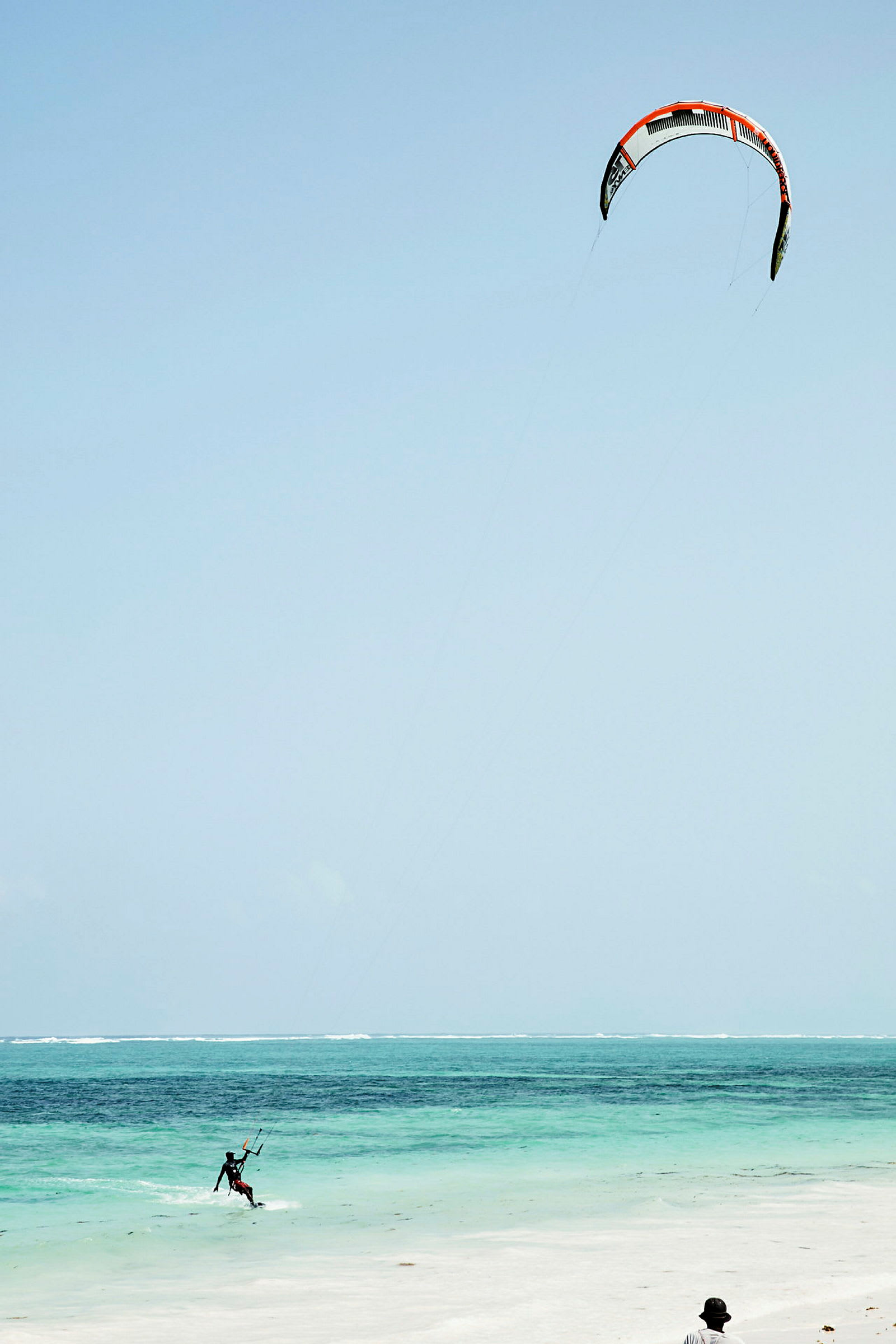 En person driver med kitesurfing på en klarblå havsstrand. (AI-generert tekst)