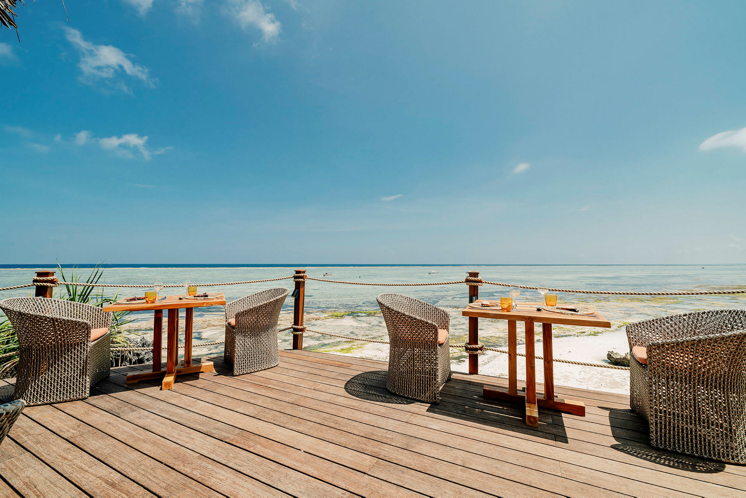 Terrasse med bord og stoler med utsikt over havet, under en blå himmel. (AI-generert tekst)
