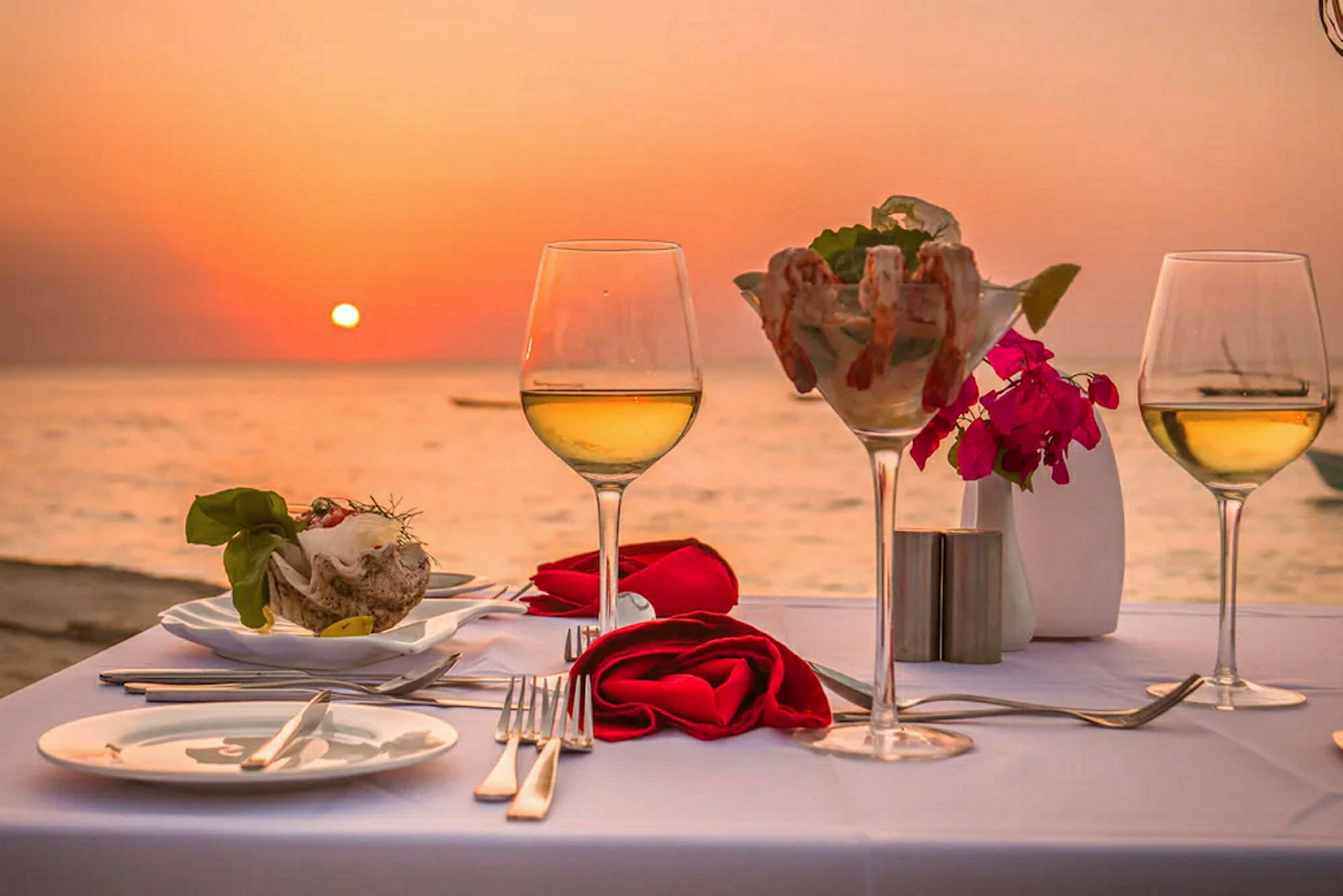 Dekket bord med vin og skalldyr med solnedgang over havet i bakgrunnen. (AI-generert tekst)