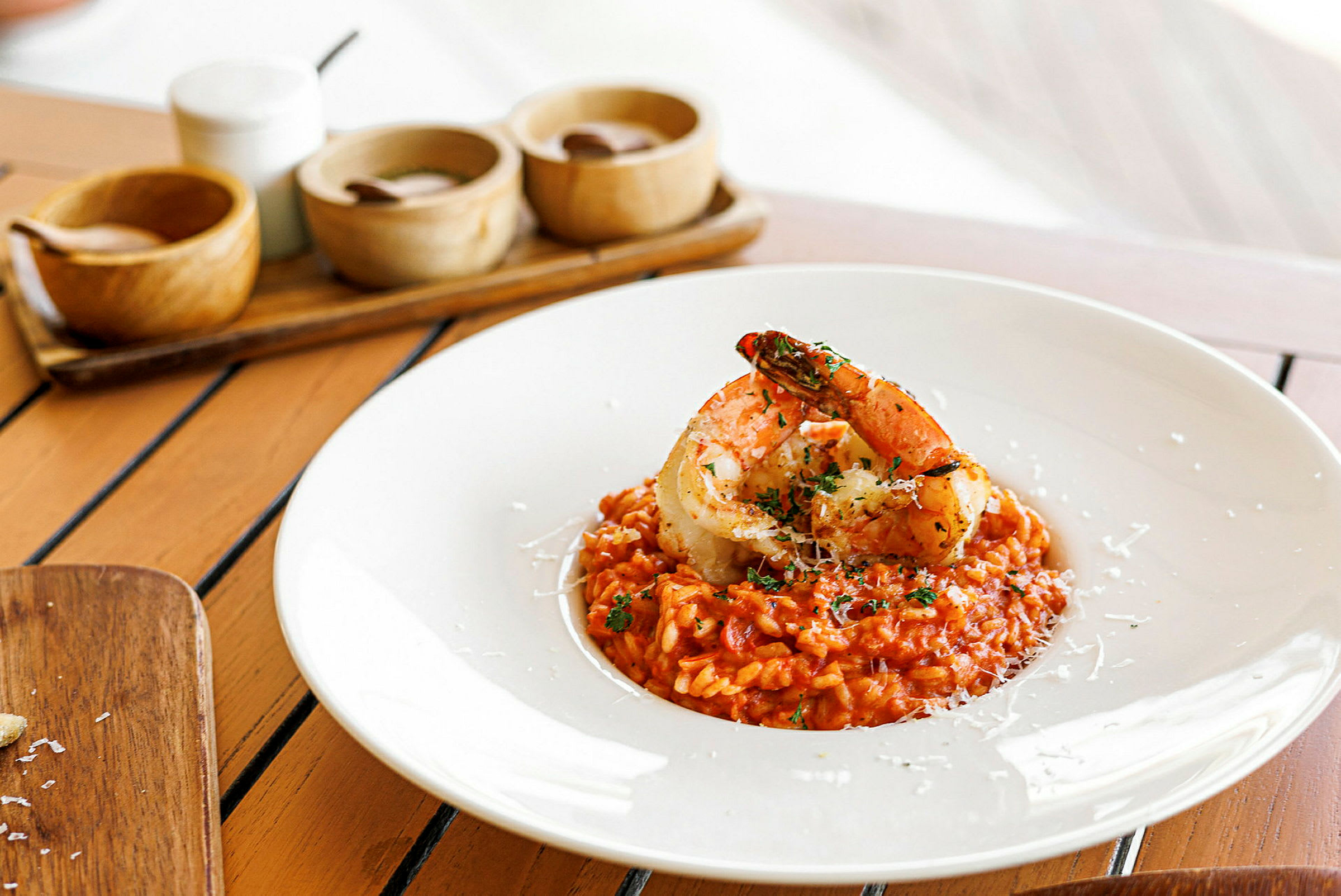 En tallerken med risotto toppet med store reker på et bord. (AI-generert tekst)