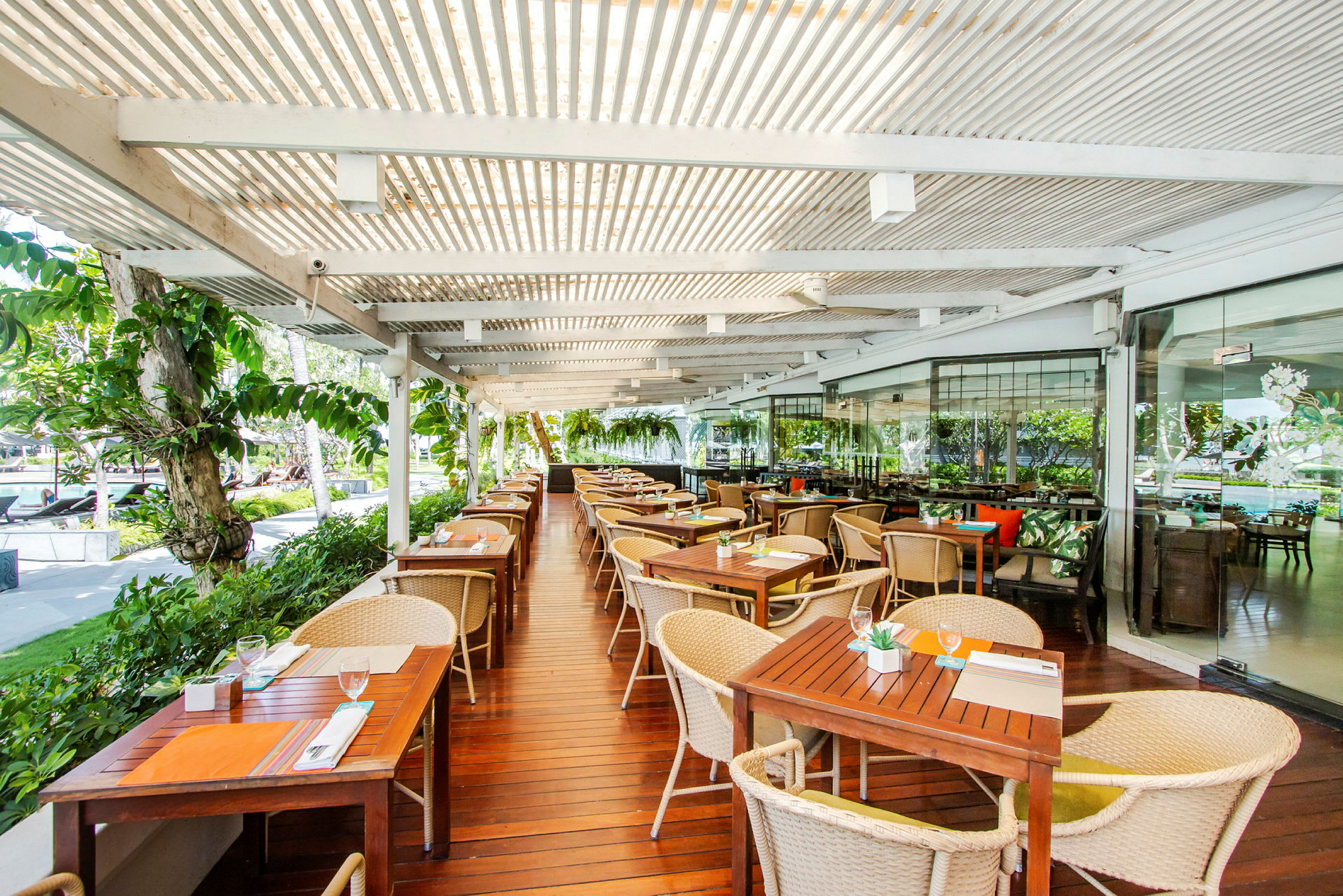 Utendørsrestaurant med trebord og stoler under en overbygd pergola. (AI-generert tekst)