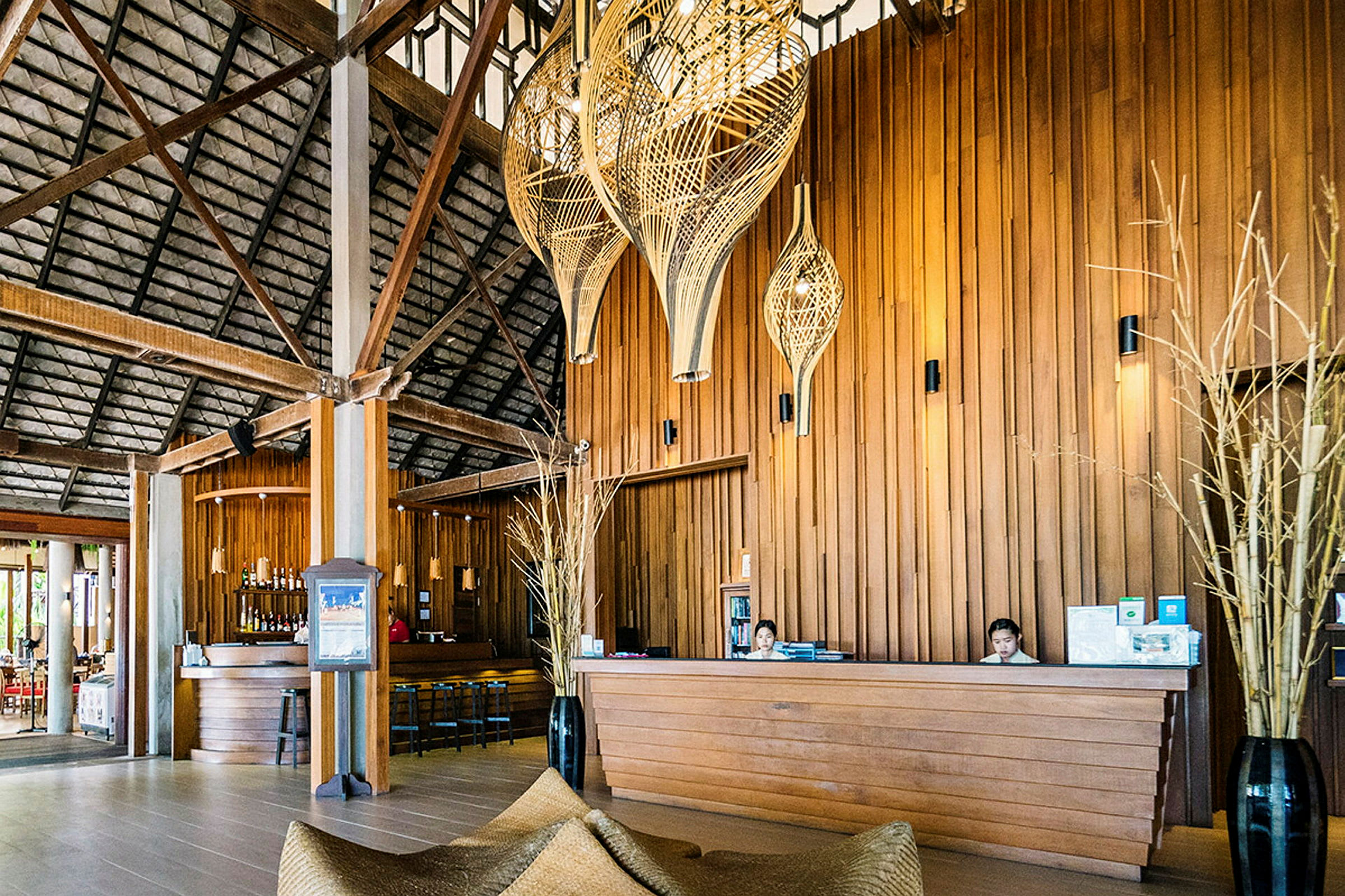 Resepsjonen på en tropisk resort med trepanel, lykter og en bar i bakgrunnen. (AI-generert tekst)