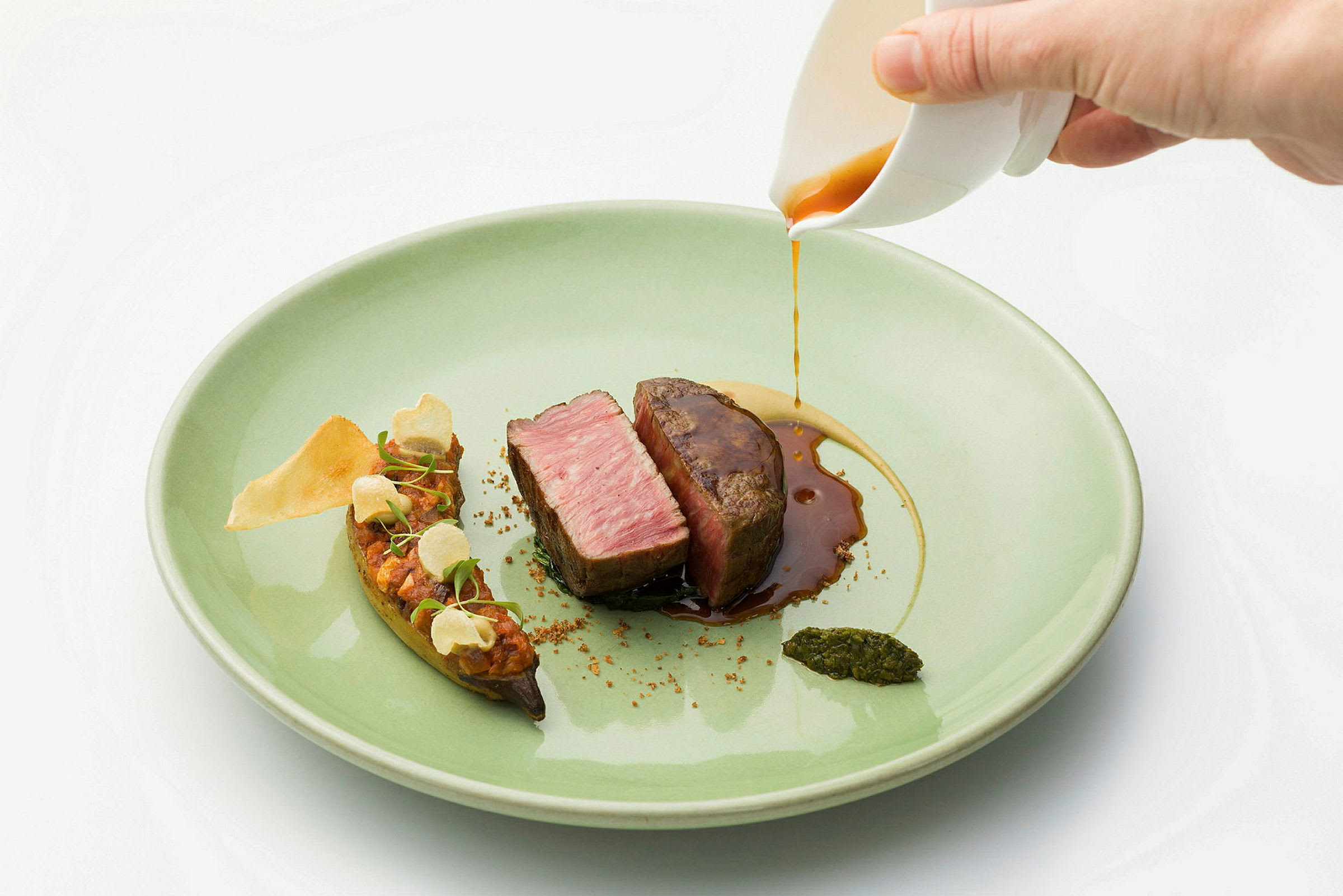 En tallerken med en kjøttbit skåret i skiver med saus som helles over, sammen med garnityr og puré. (AI-generert tekst)