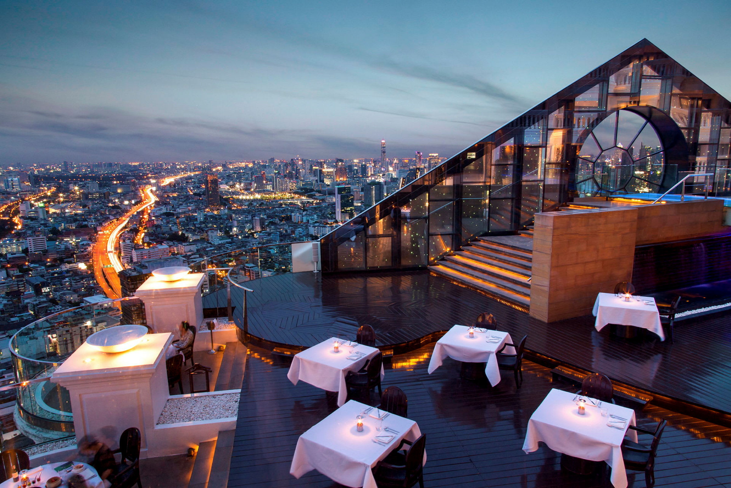 Takrestaurant med belysning og utsikt over byens skyline i kveldssolens skinn. (AI-generert tekst)