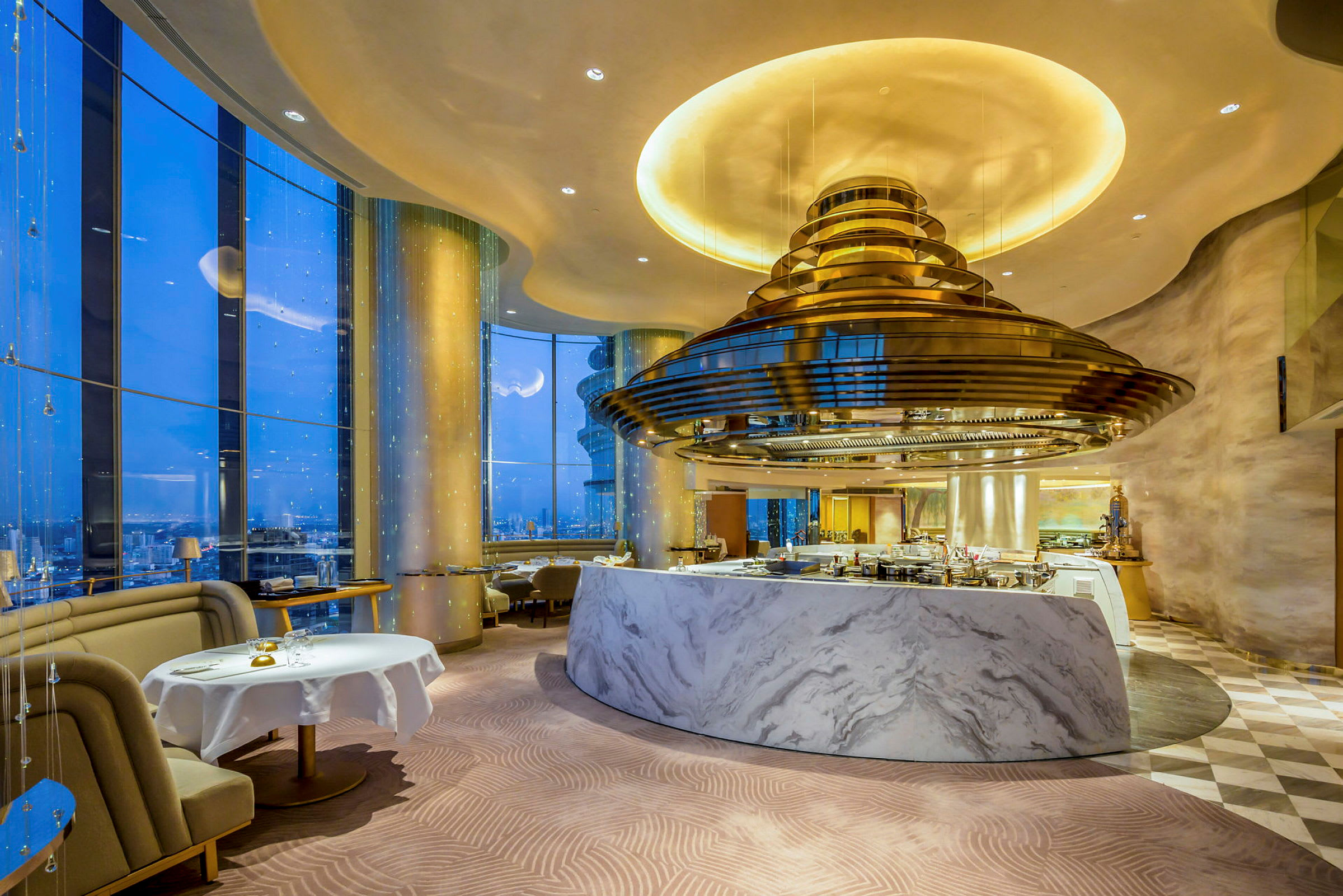 En elegant restaurant med marmorinteriør og store vinduer som gir utsikt over byens nattlandskap. (AI-generert tekst)
