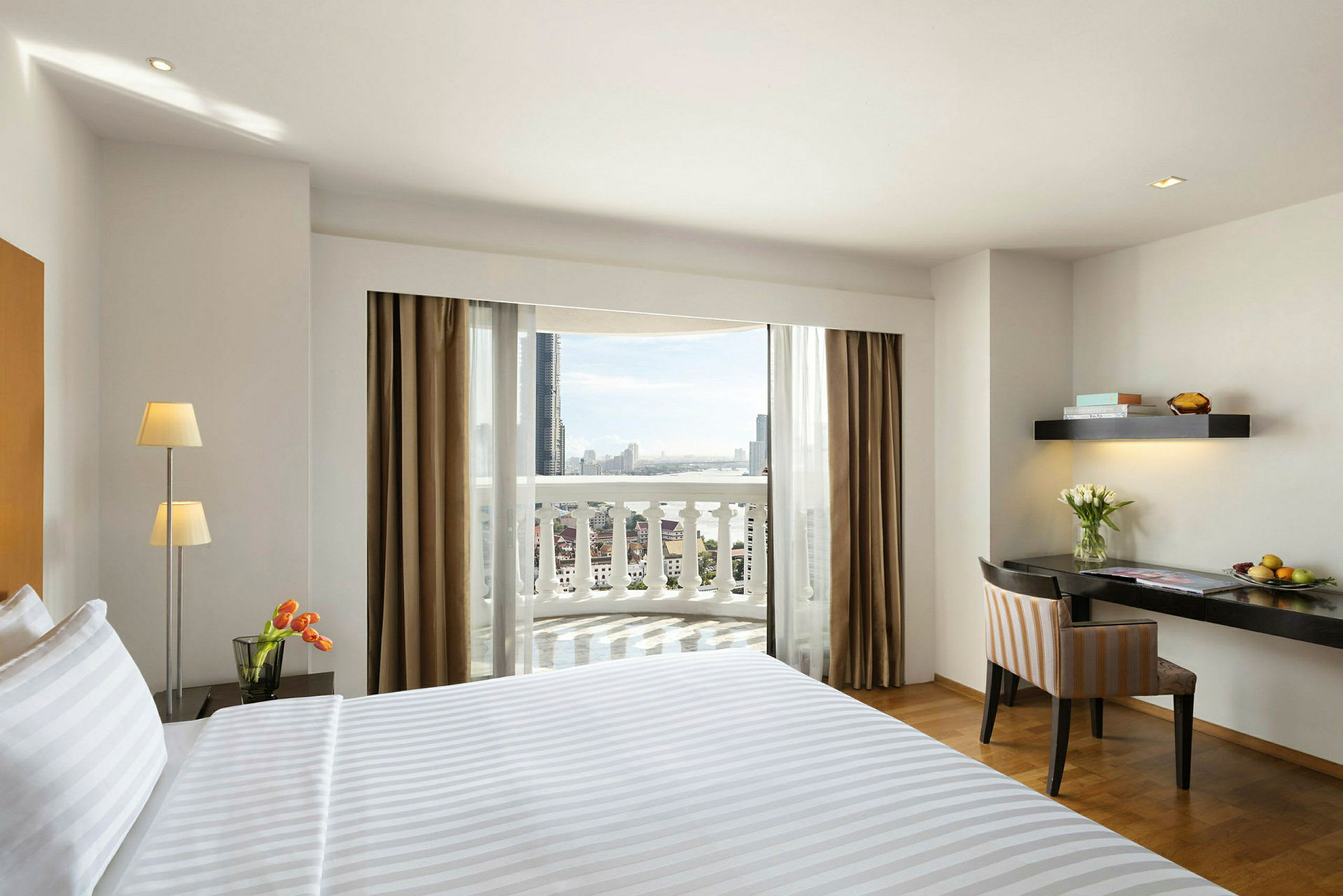Hotellrom med en oppredd seng, skrivebord og noen blomster, samt en balkong med utsikt. (AI-generert tekst)