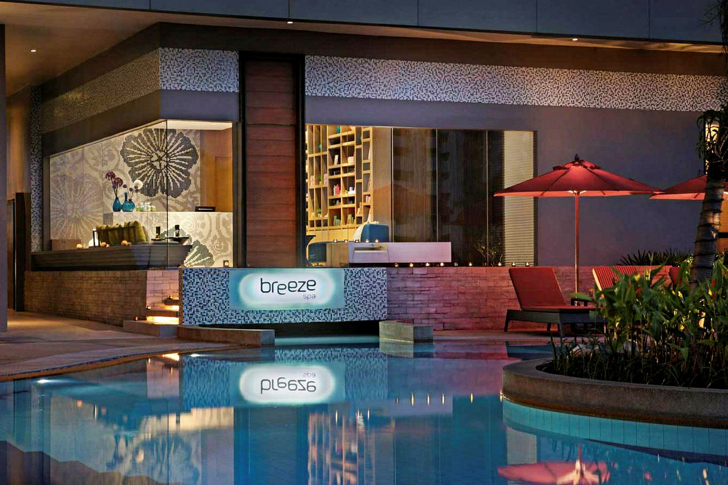 Spaområde med skiltet "Breeze Spa", samt røde parasoller og solsenger ved et basseng. (AI-generert tekst)