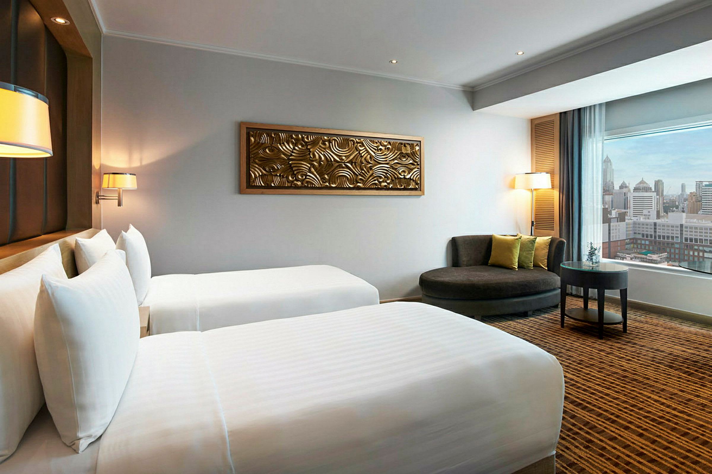 Hotellrom med to enkeltsenger, dekorasjon på veggen og sitteområde med utsikt over byen gjennom et vindu. (AI-generert tekst)