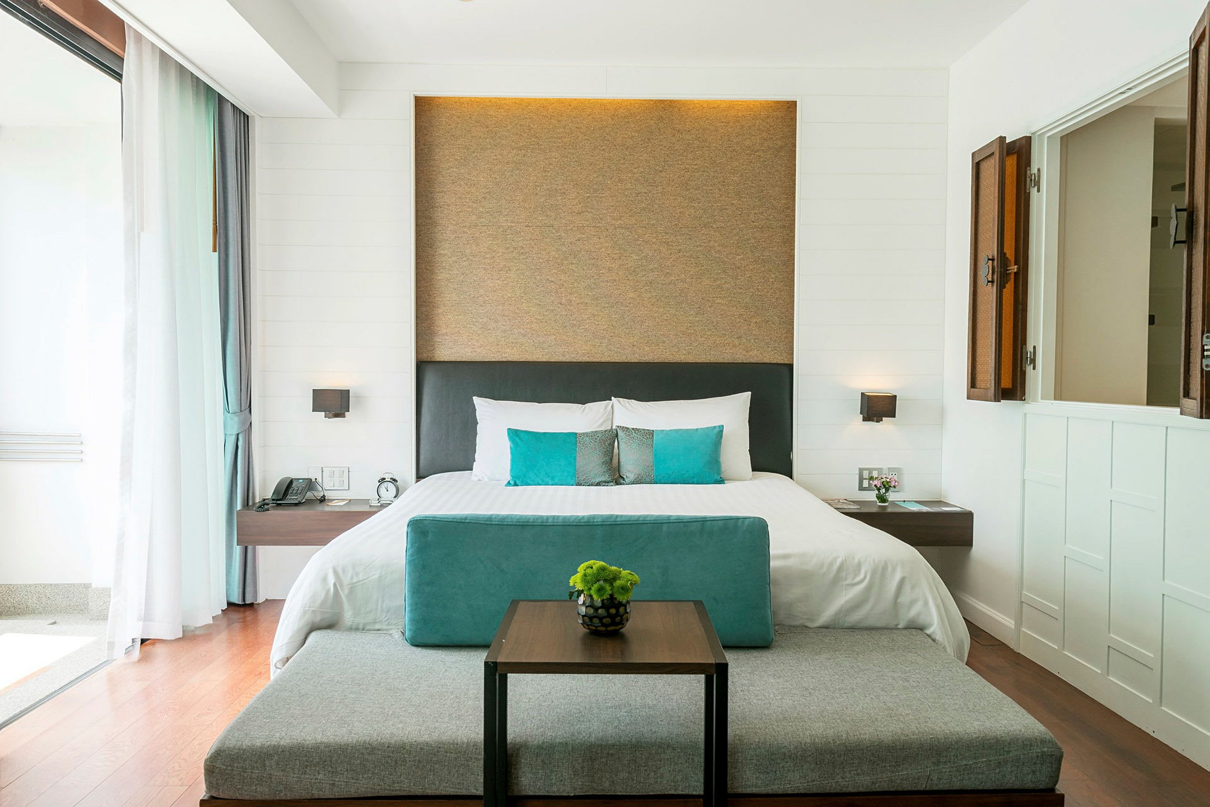 Et moderne hotellrom med en dobbeltseng, pynteputer og et lite bord med en vase. (AI-generert tekst)