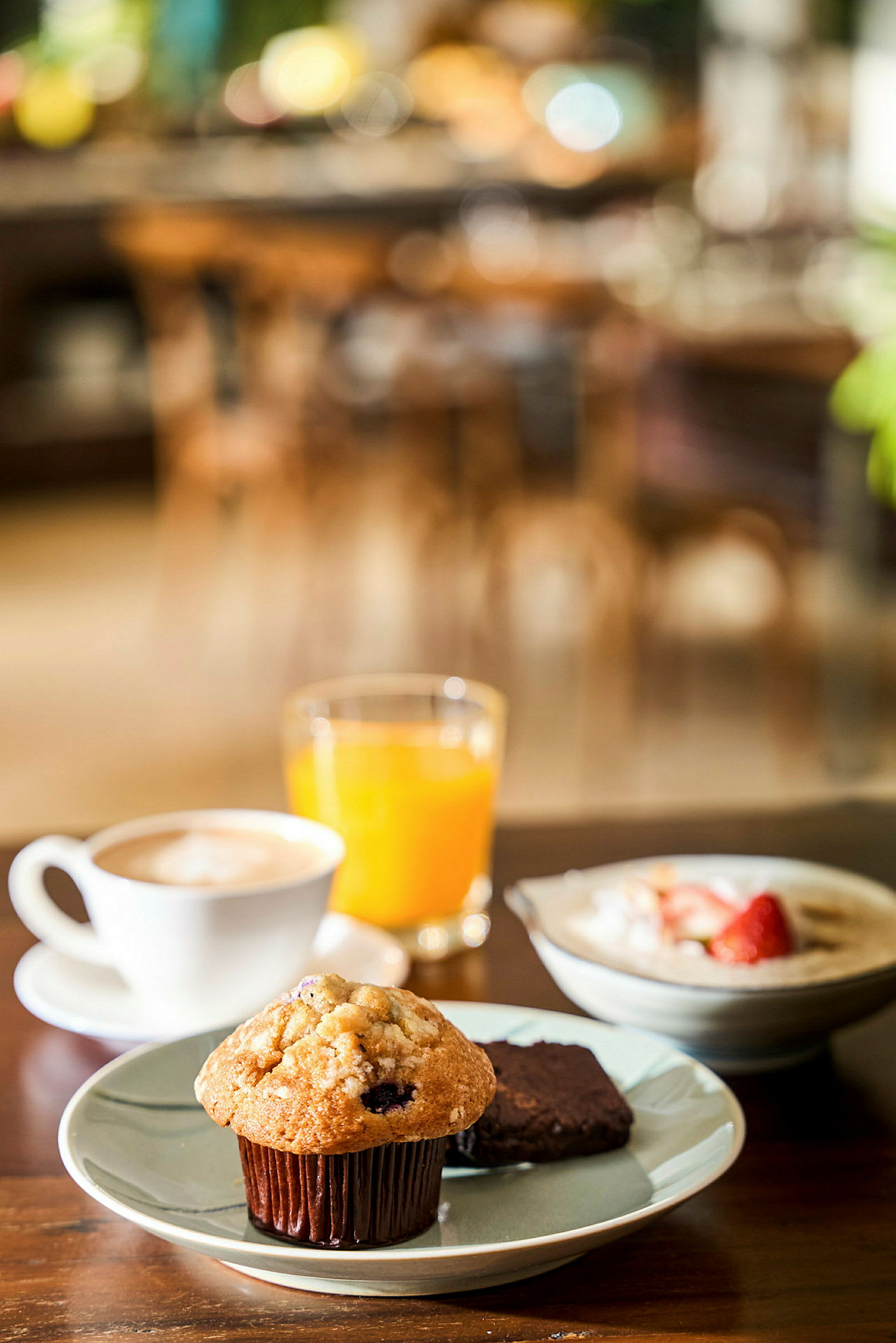 Frokost med muffins, brownie, kaffe, appelsinjuice og tallerken med jordbær. (AI-generert tekst)