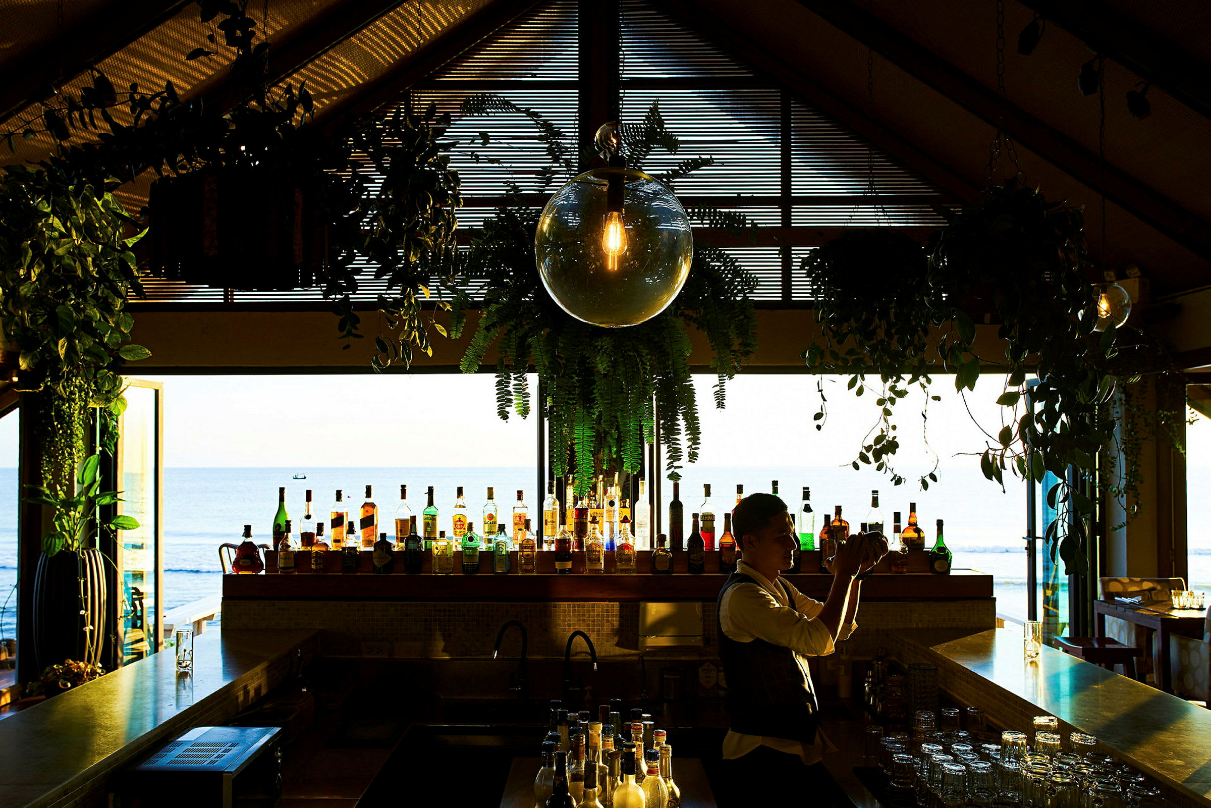 En bar med ulike flasker og dekorasjoner i et rom med utsikt ut mot havet. (AI-generert tekst)