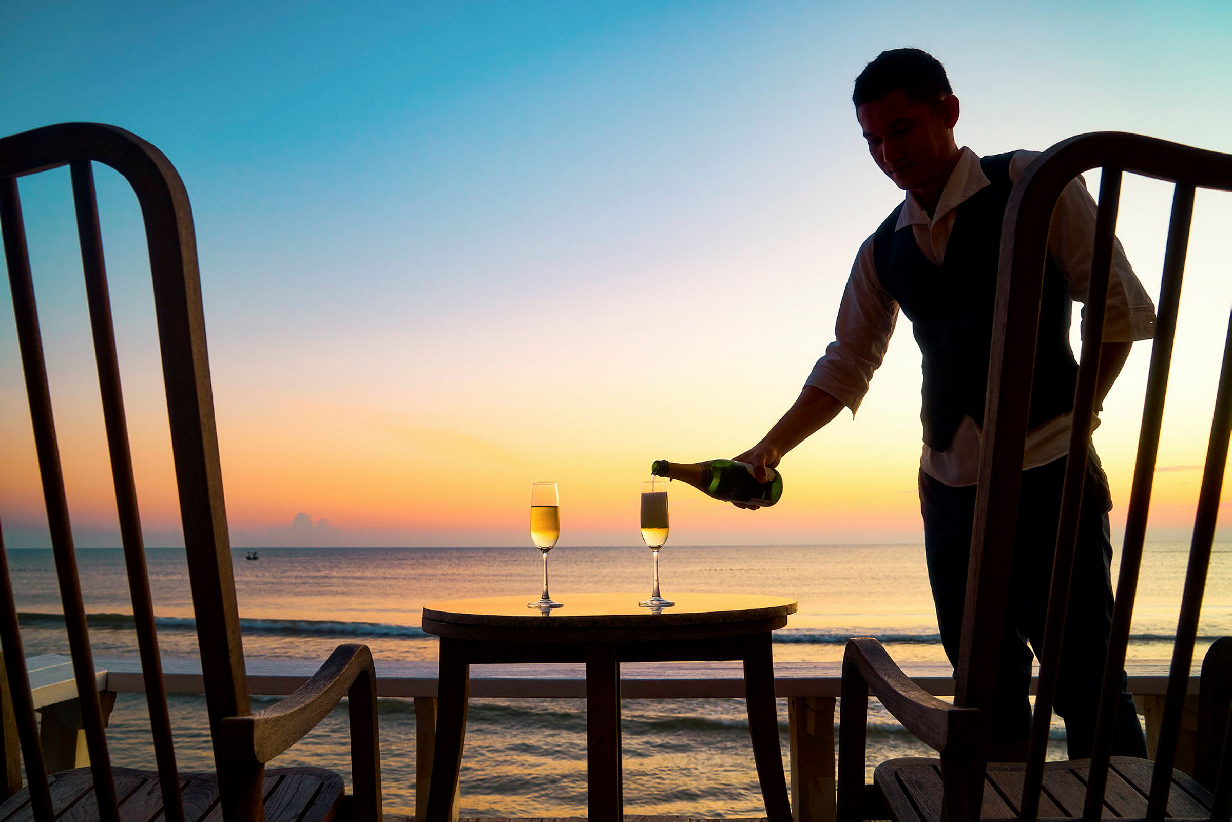 To glass champagne på et bord med havutsikt under solnedgang. (AI-generert tekst)
