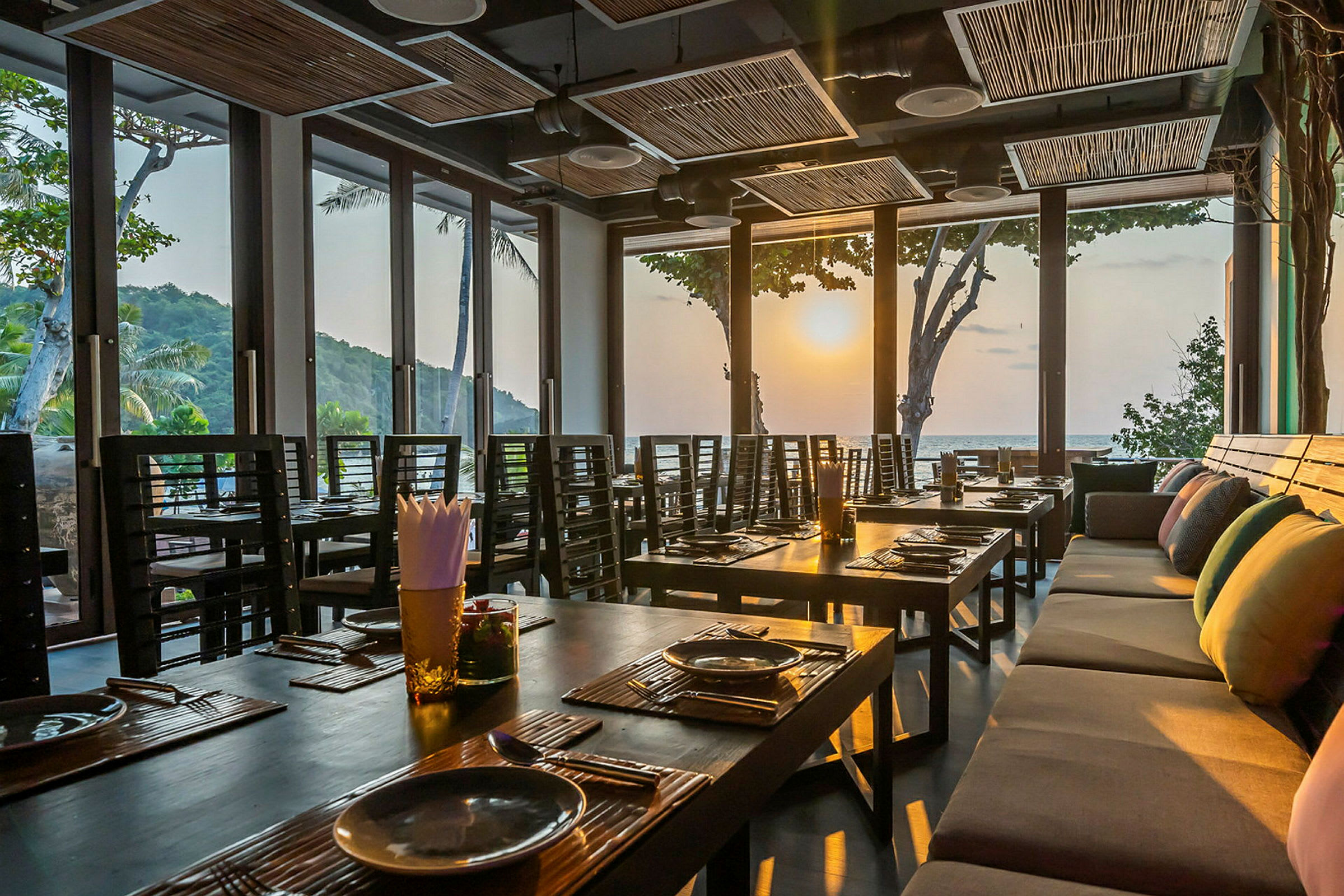 Interiør av en restaurant med dekkede bord og store vinduer som slipper inn lyset fra solnedgangen. (AI-generert tekst)