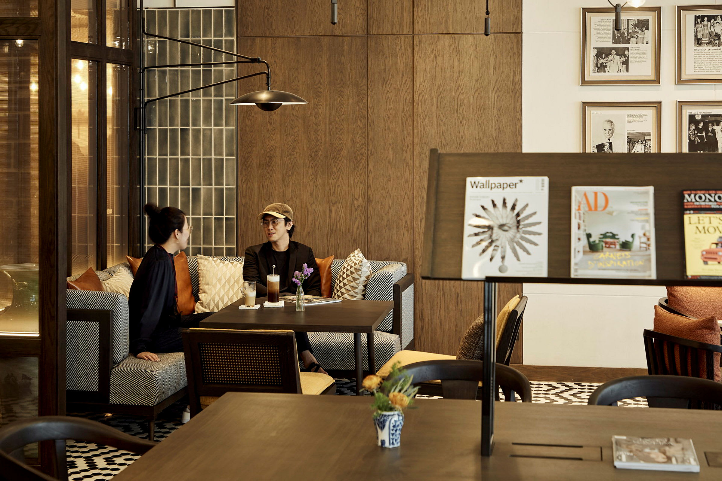 Et par personer samtaler ved et bord i et stilrent innredet kafé, med moderne møbler og dekorativ belysning. (AI-generert tekst)