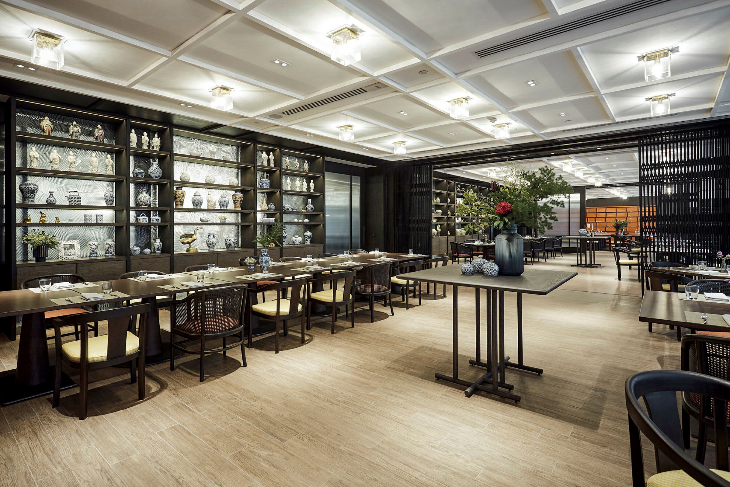 En spisestue med elegante bord, stoler og hyller fylt med dekorative gjenstander og porselen. (AI-generert tekst)