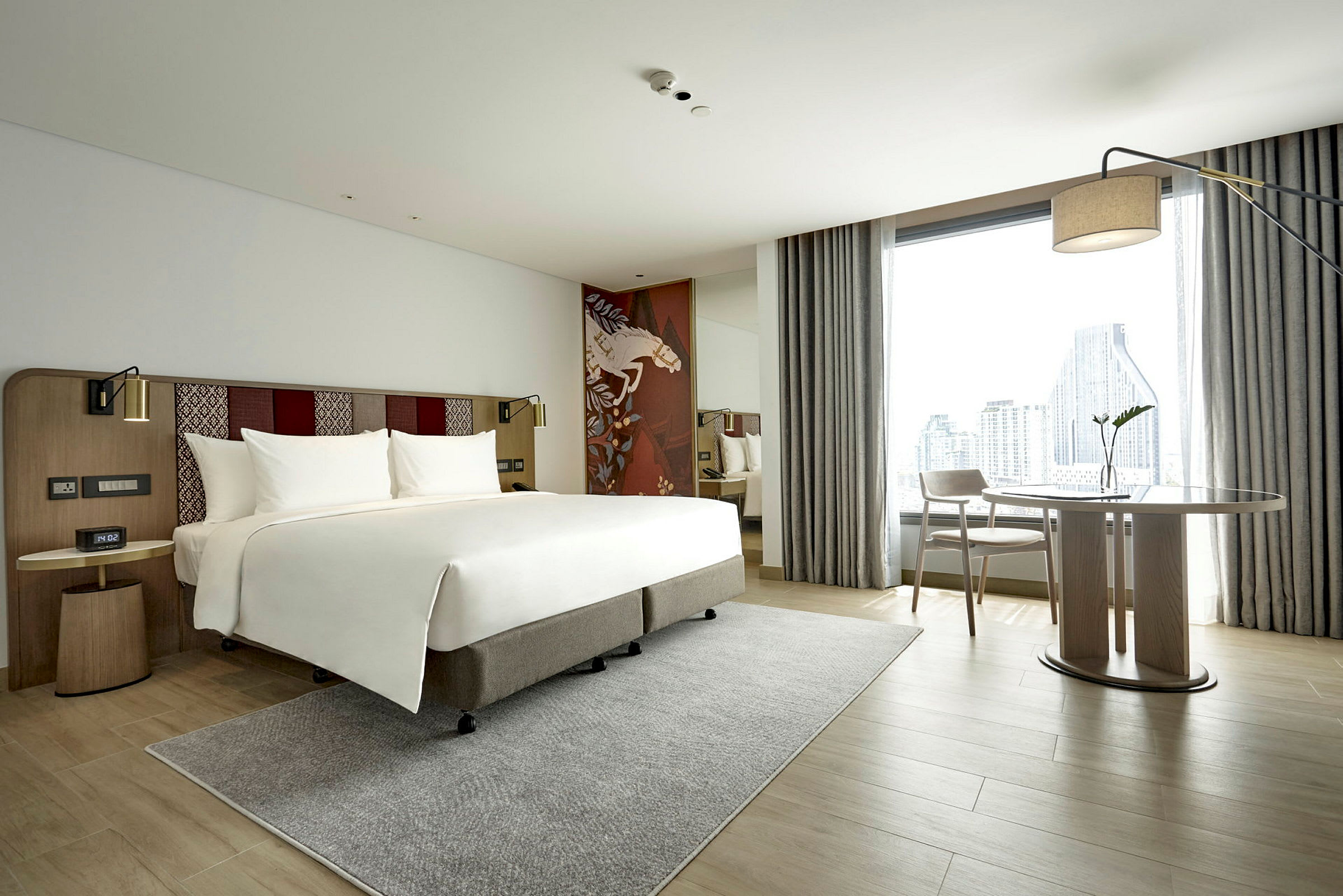 Moderne hotellrom med en dobbeltseng, skrivebord og utsikt over en by gjennom et stort vindu. (AI-generert tekst)