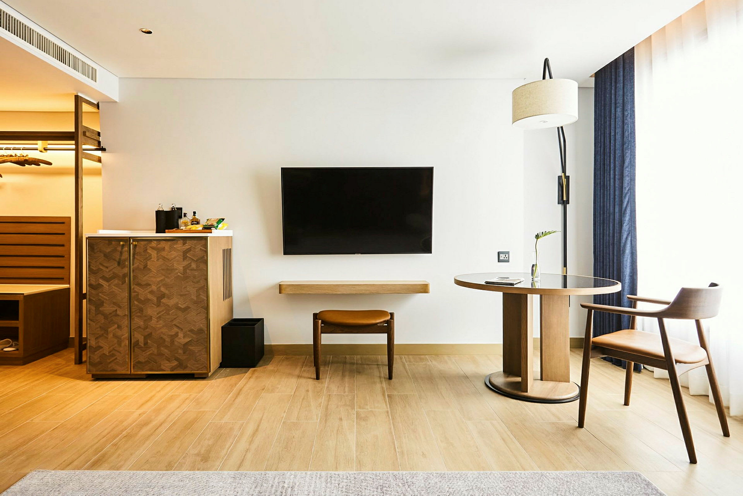 Et hotellrom med tremøbler, en TV på veggen og et stort vindu med gardiner. (AI-generert tekst)