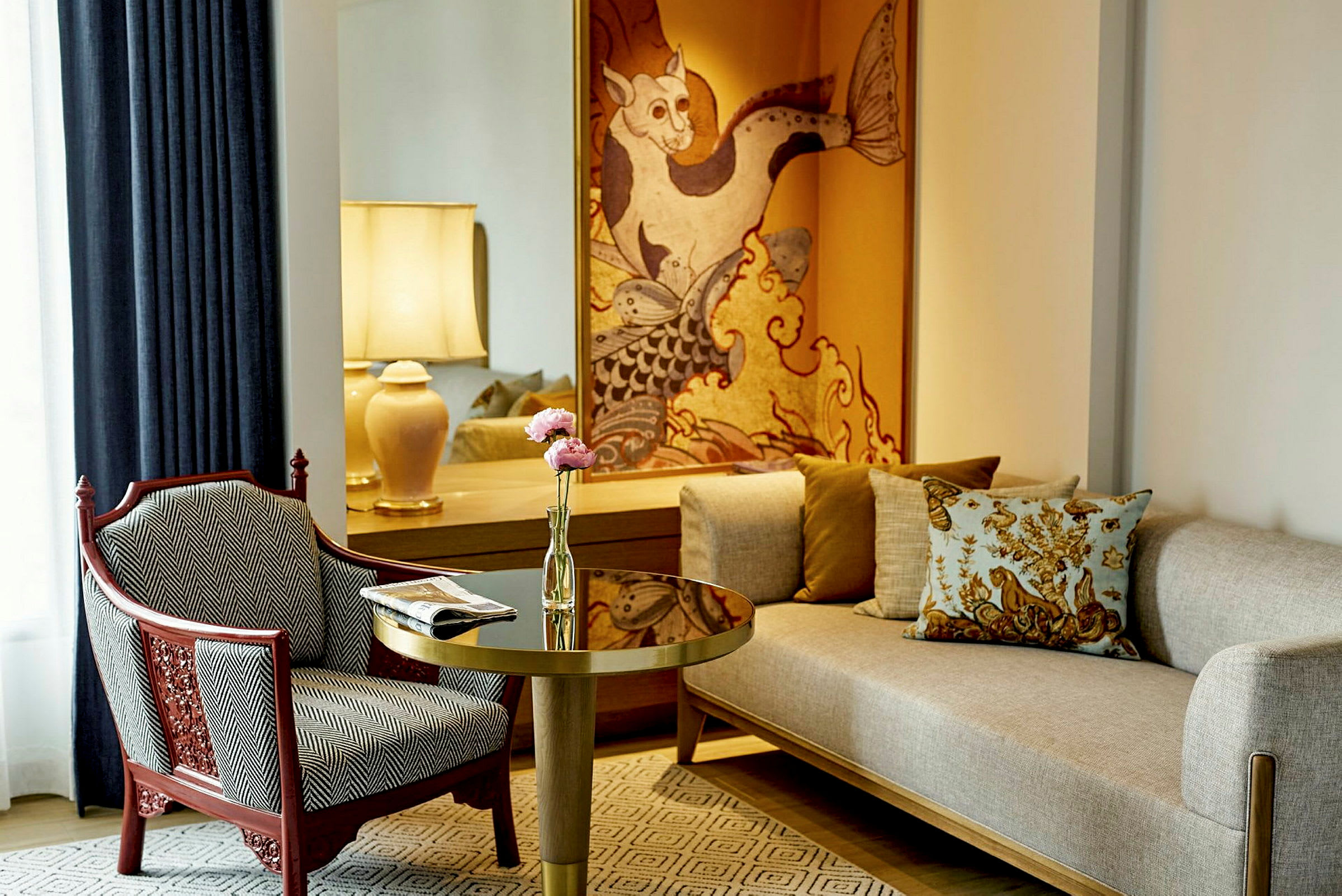 Et elegant rom med en lys sofa, en mønstret lenestol, et bord med blomster og en bordlampe samt dekorativ kunst på veggen. (AI-generert tekst)