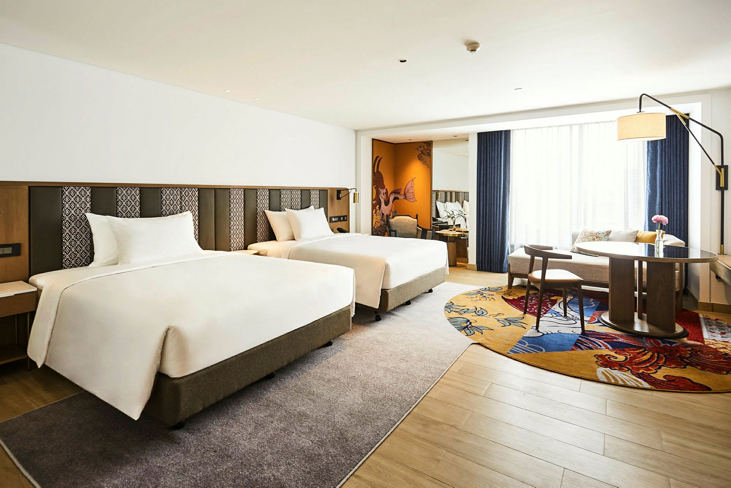 Hotellrom med to separate senger, et bord og stoler samt sofakrok. (AI-generert tekst)