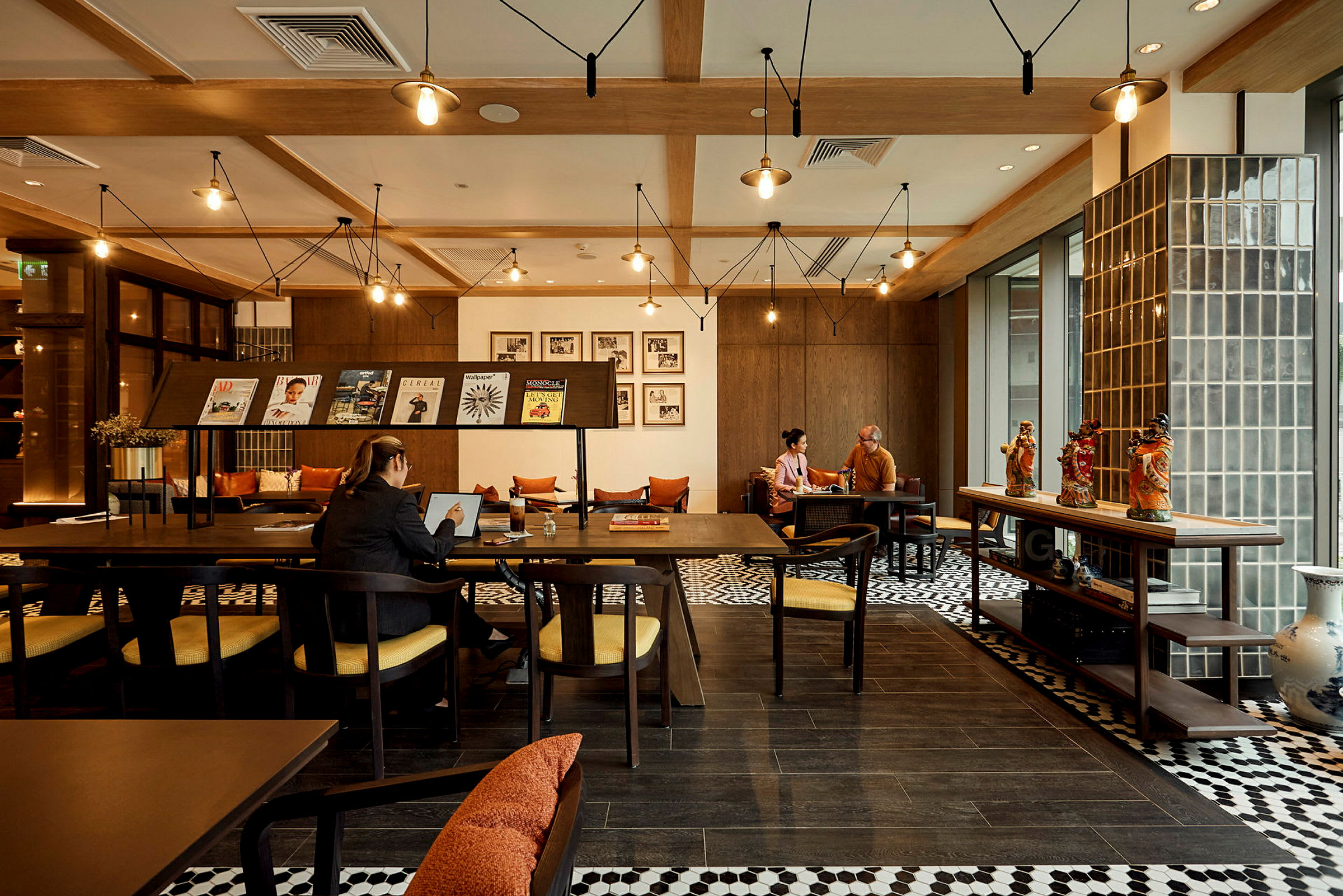 Interiør av en kafé eller arbeidsområde med tremøbler, dekorasjoner på bordet og personer som arbeider eller samtaler. (AI-generert tekst)