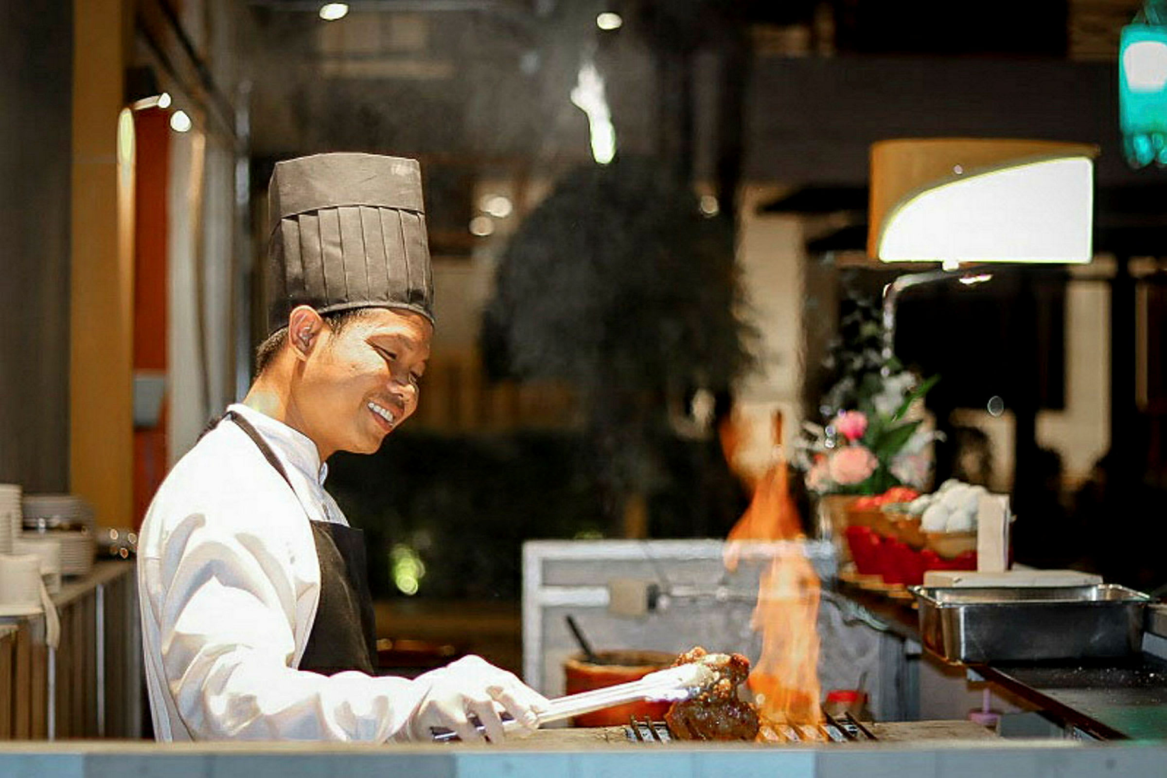 En kokk står ved en grill med åpen flamme og tilbereder et måltid. (AI-generert tekst)