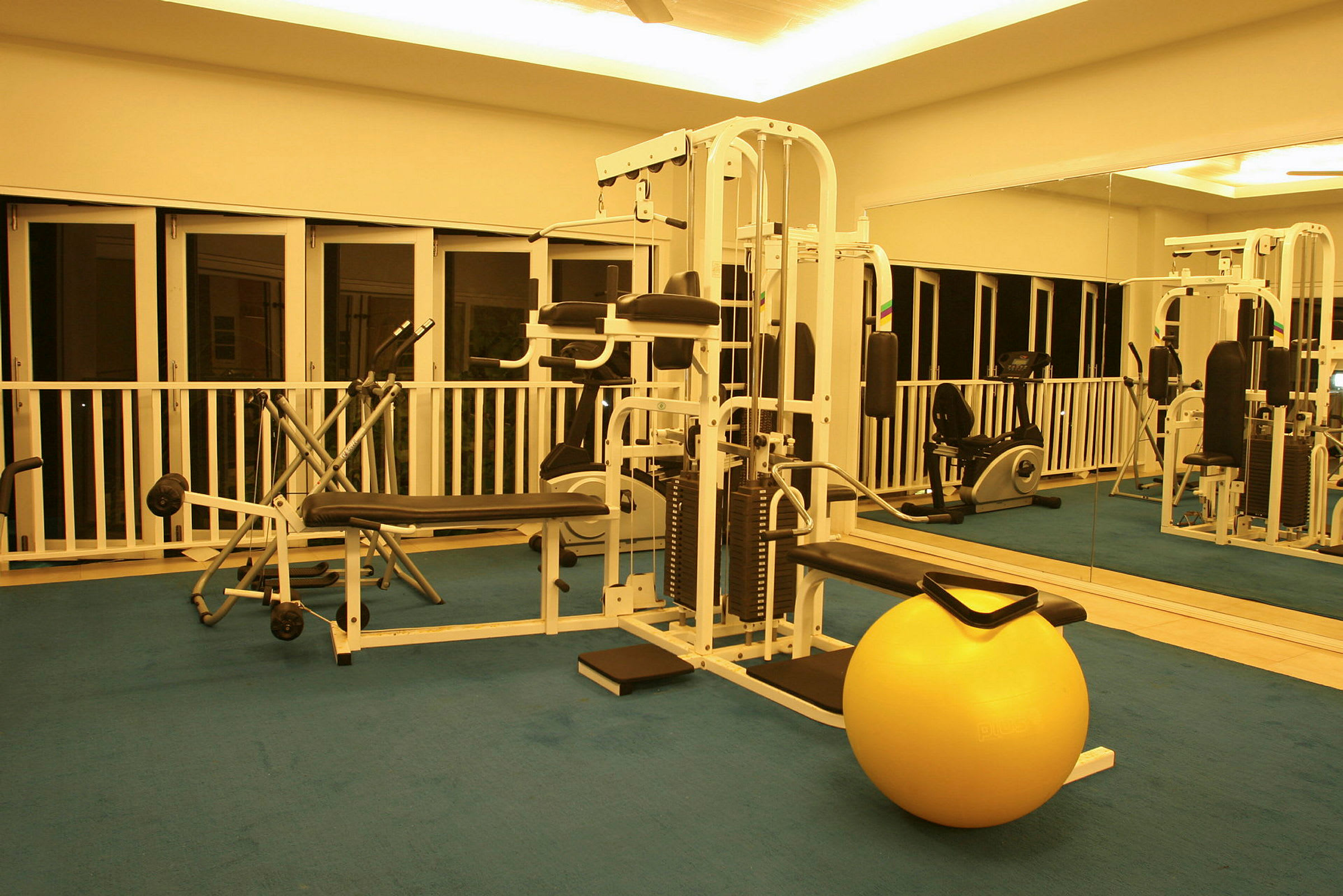 Interiør av et treningsstudio med treningsutstyr og en gul balanseball på gulvet. (AI-generert tekst)