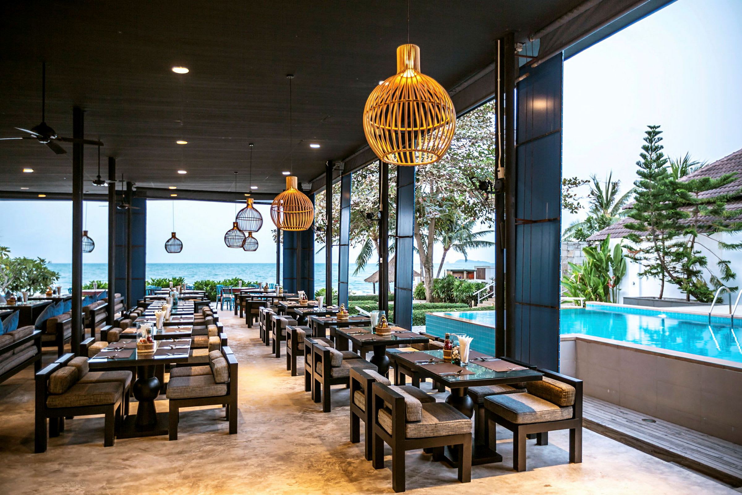 En utendørs restaurant med sitteplasser ved et basseng, med havet i bakgrunnen. (AI-generert tekst)