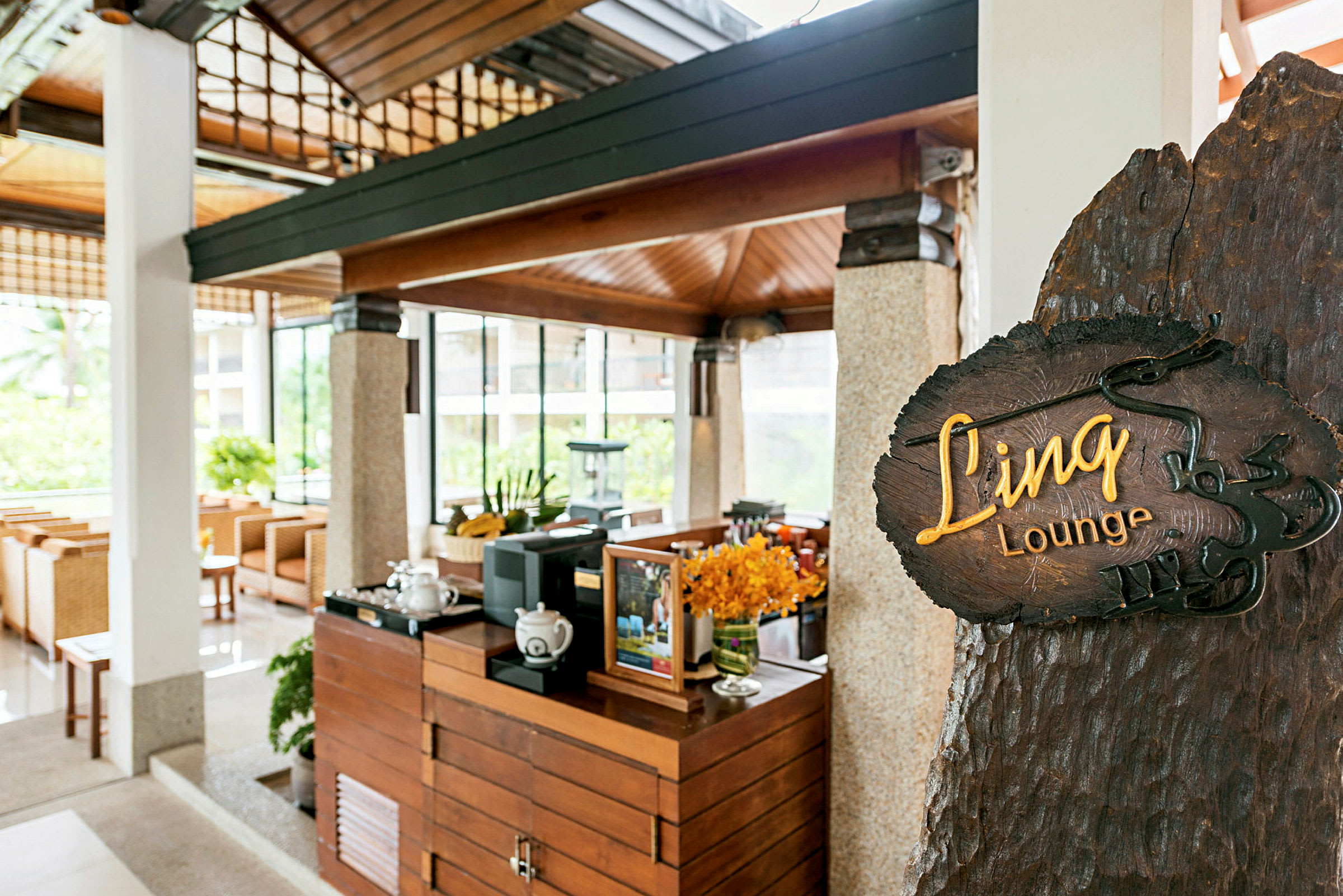 Et bilde av et loungeinteriør med et trebord og termokanneområder, dekorert med blomster. I forgrunnen er et skilt som viser navnet 'Linq Lounge'. (AI-generert tekst)