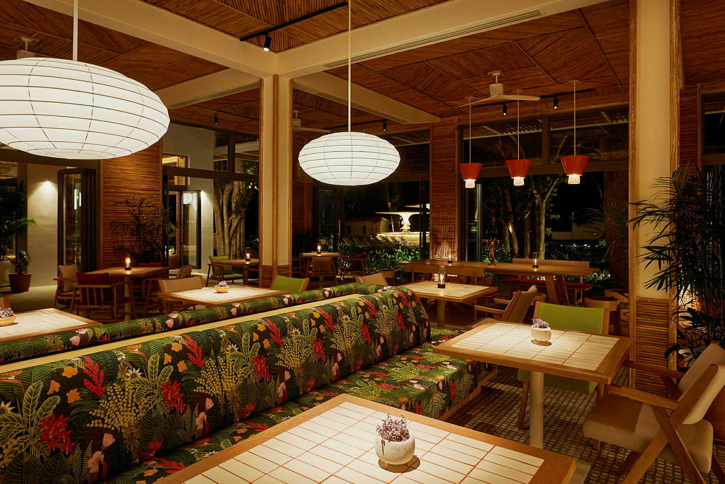 Interiøret av en restaurant med treverk, planter og opplyste bord. Stoler og sofaer med fargerike mønstre er synlige. (AI-generert tekst)