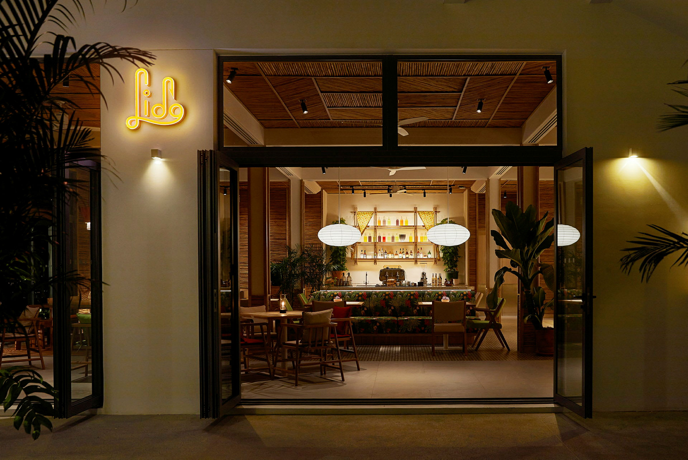 En åpen dør til en restaurant med moderne interiør, med planter og en opplyst bardisk inni. (AI-generert tekst)