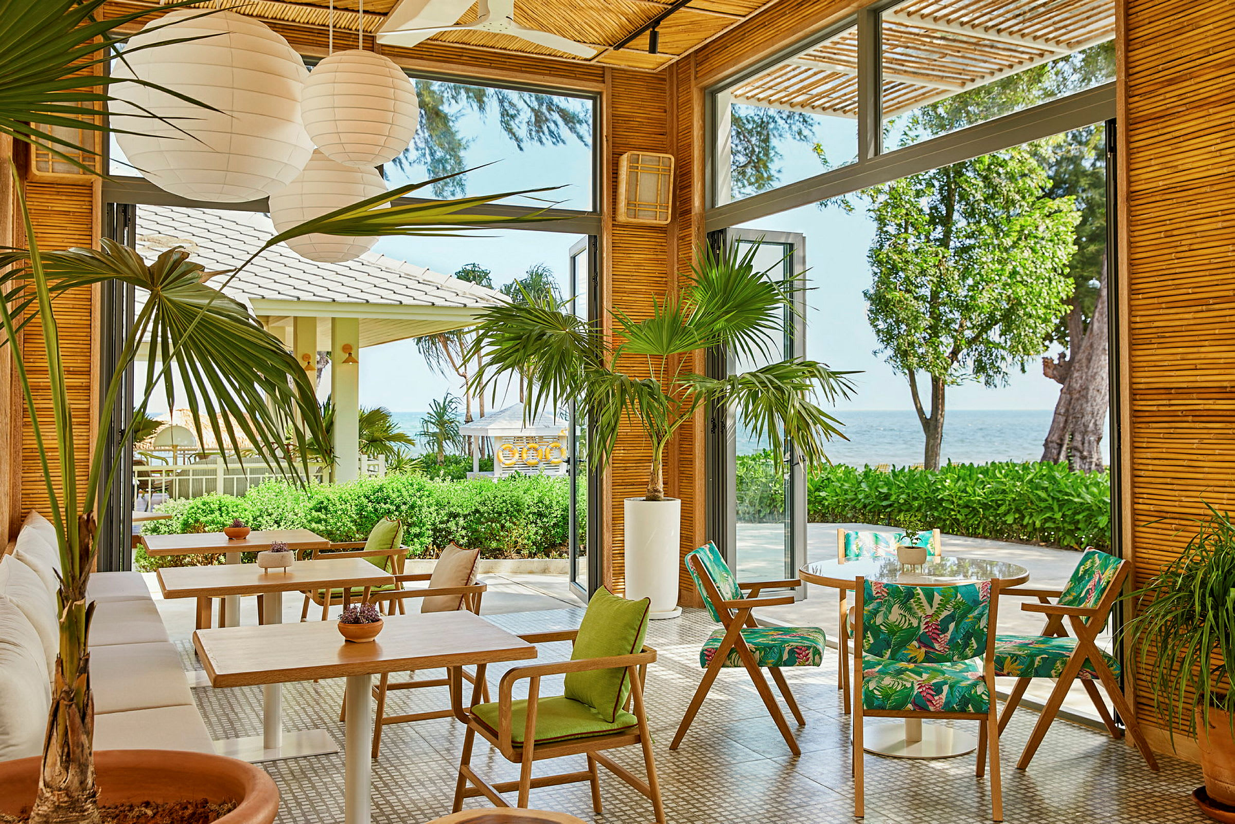 Restaurant med åpne glassvegger, grønne planter og utsikt mot havet. (AI-generert tekst)