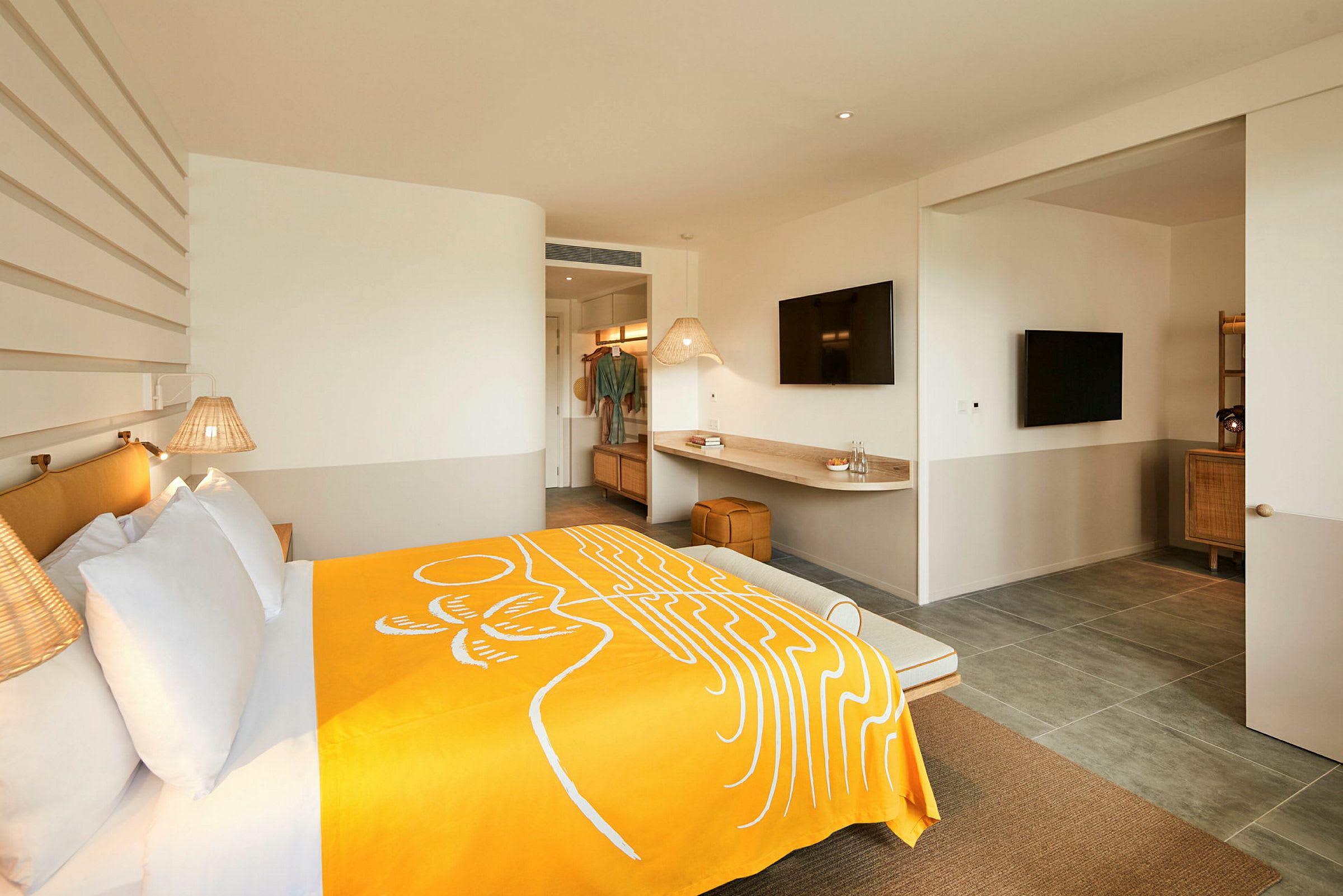 Et moderne hotellrom med en bred seng dekket med et gult teppe, veggmonterte lamper og en skrivebordsoverflate med en TV over. (AI-generert tekst)