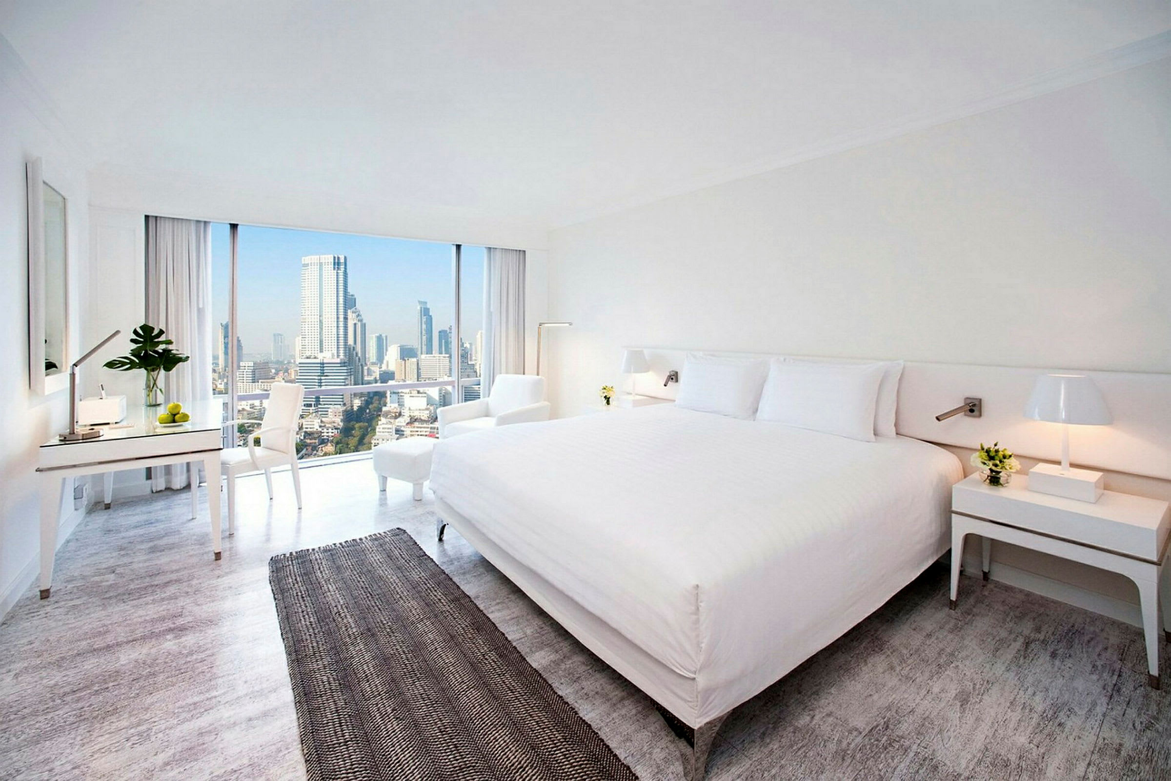 Hotellrom med moderne innredning, stor seng og utsikt over byens skyline gjennom store vinduer. (AI-generert tekst)