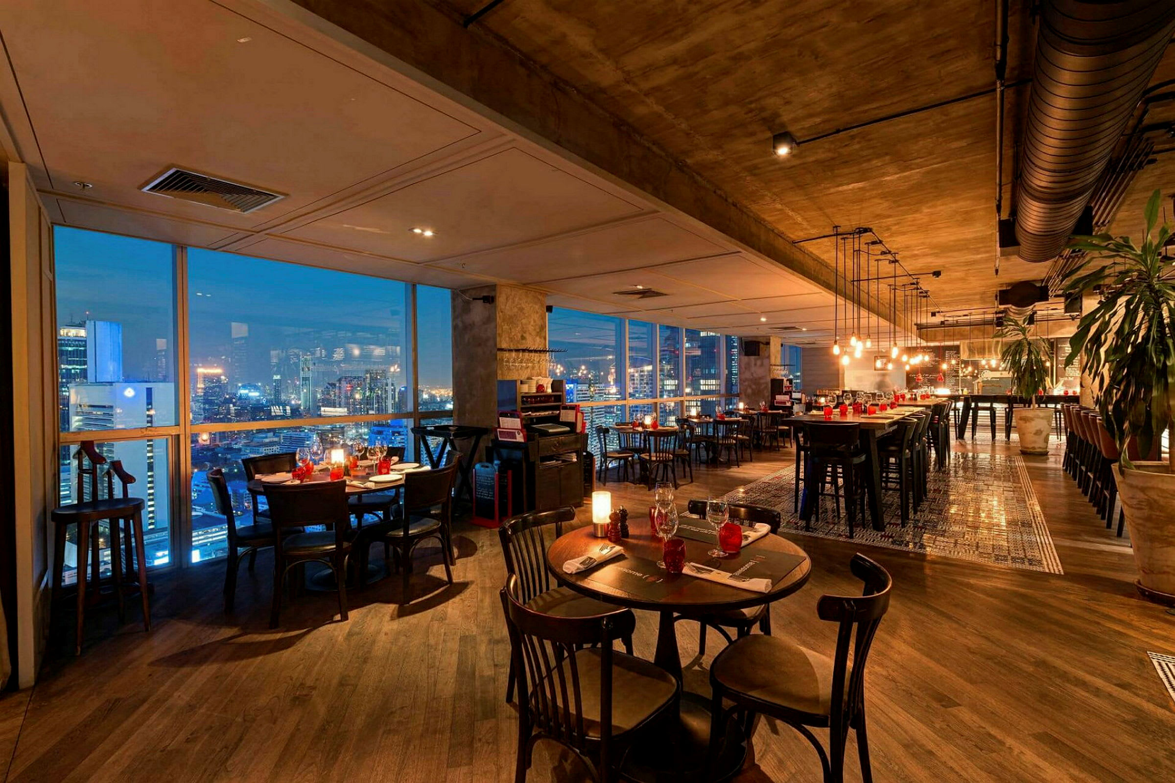 En elegant restaurant med moderne møbler, vinduer som viser en byutsikt om kvelden og belysning som skaper en koselig atmosfære. (AI-generert tekst)