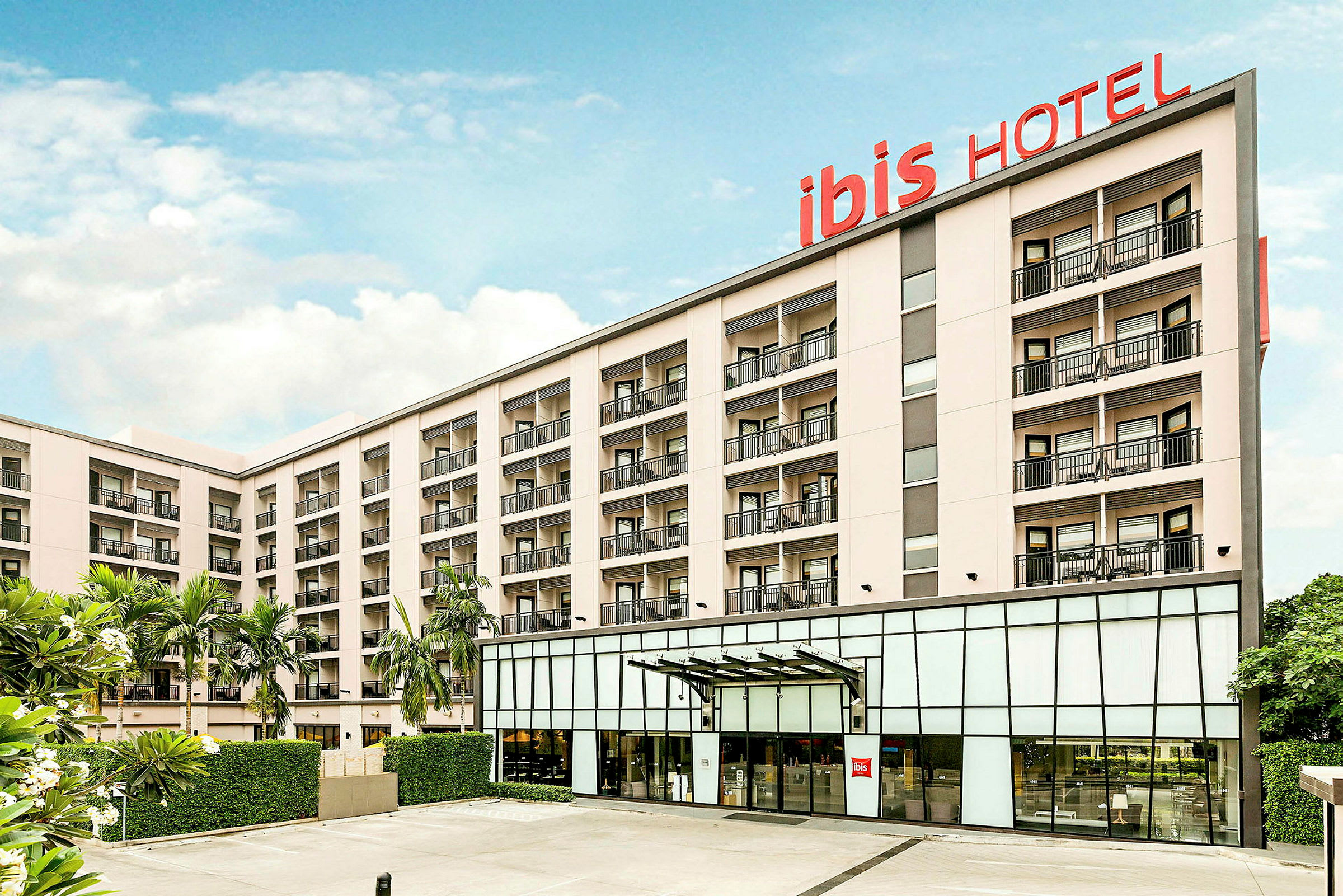 Hotellbygning med flere etasjer og balkonger, skilt med teksten 'ibis HOTEL'. (AI-generert tekst)