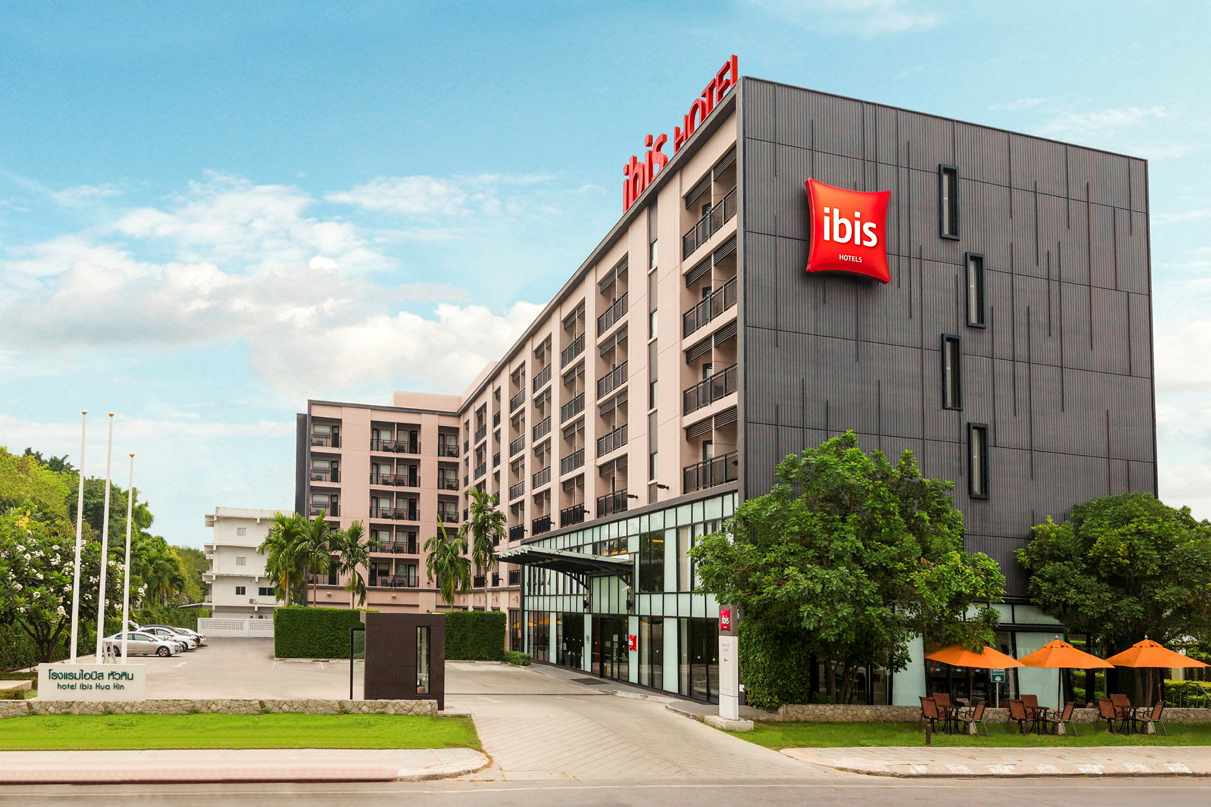 Bilde av fasaden til et fleretasjes hotell med hotellskilt og omkringliggende vegetasjon. (AI-generert tekst)