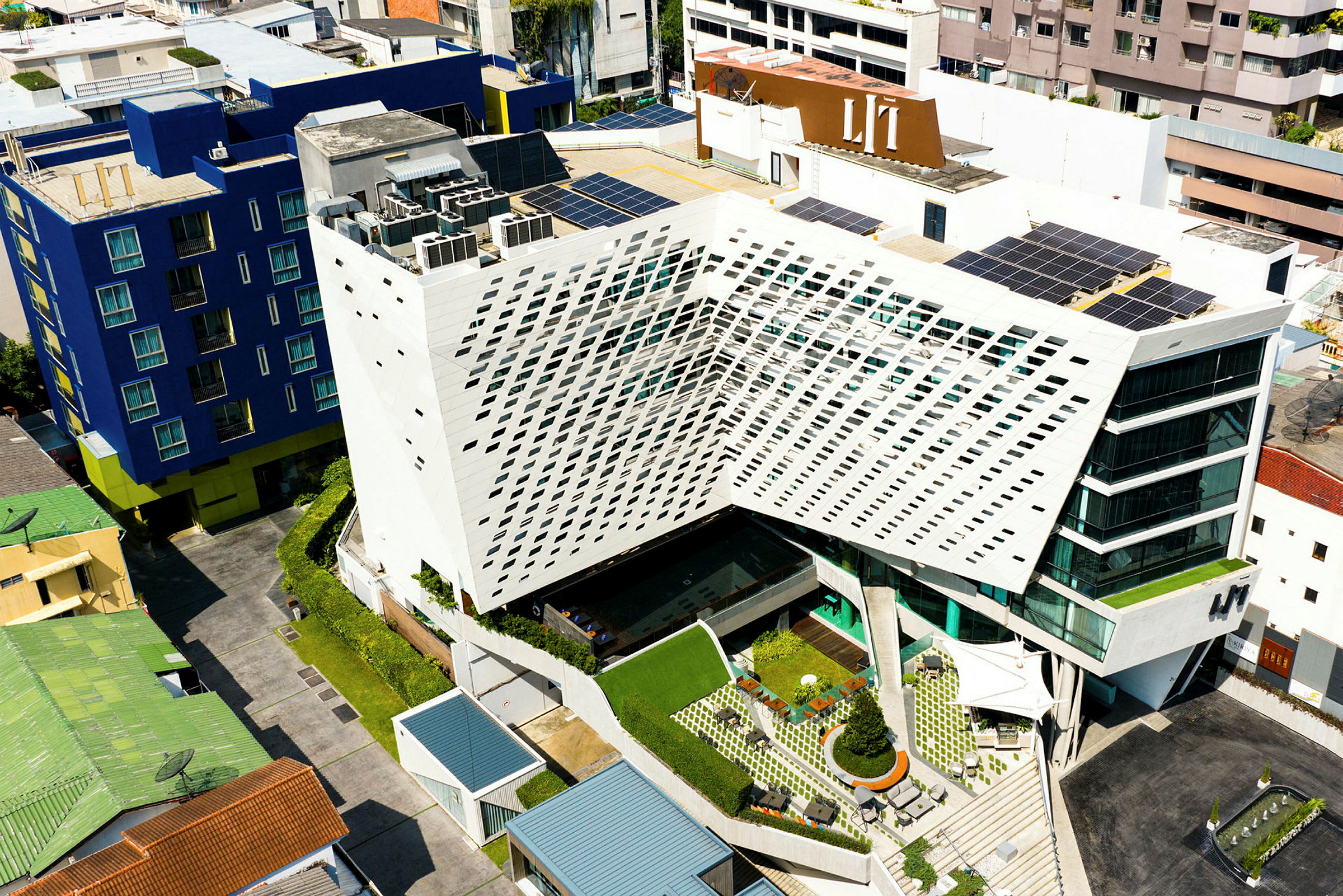 Luftfoto av en moderne bygning med geometrisk arkitektur, omgitt av andre bygninger. (AI-generert tekst)