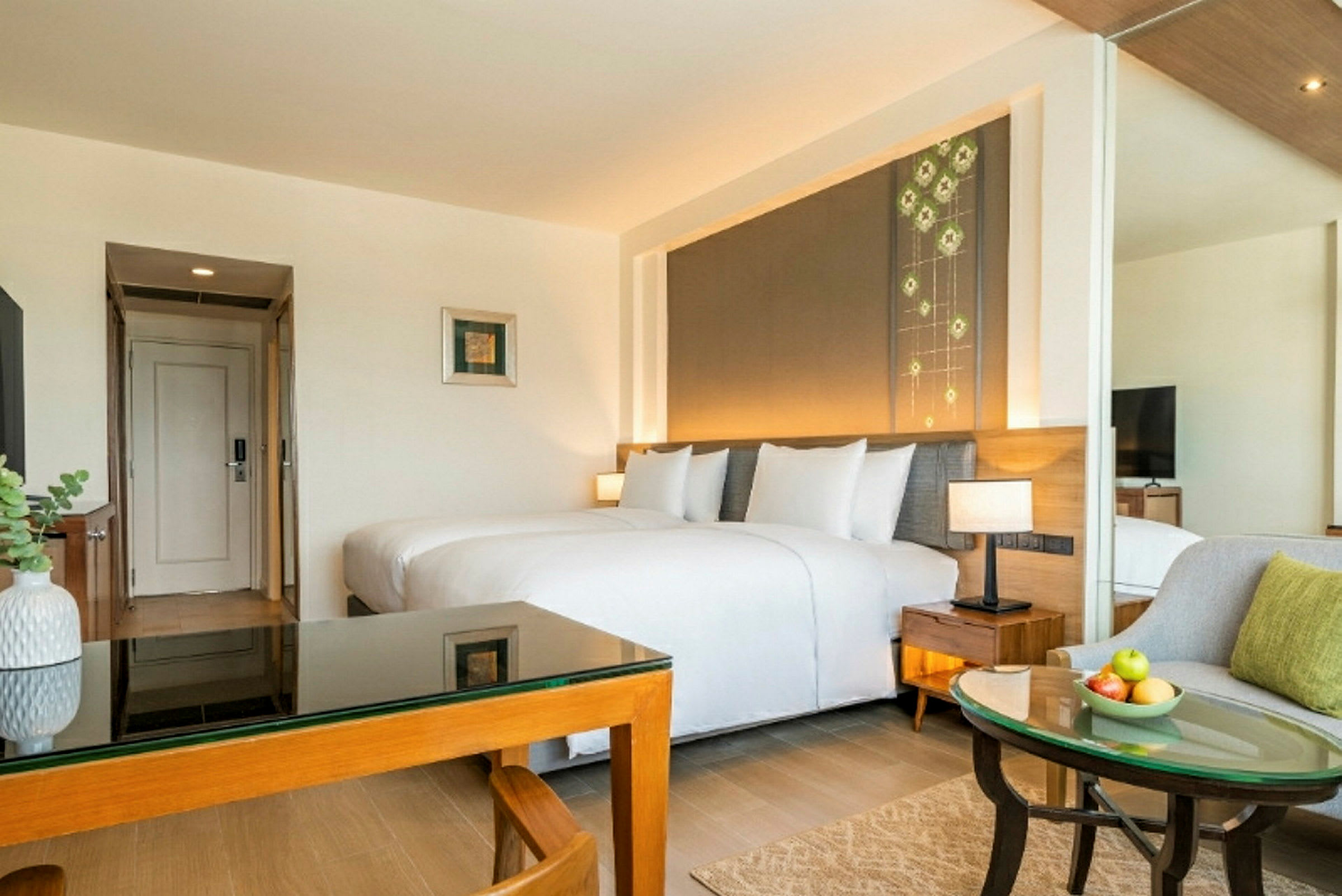Et hotellrom med en dobbeltseng, et bord med glassplate, en stol og et bilde på veggen. Rommet har lys innredning og et moderne utseende. (AI-generert tekst)