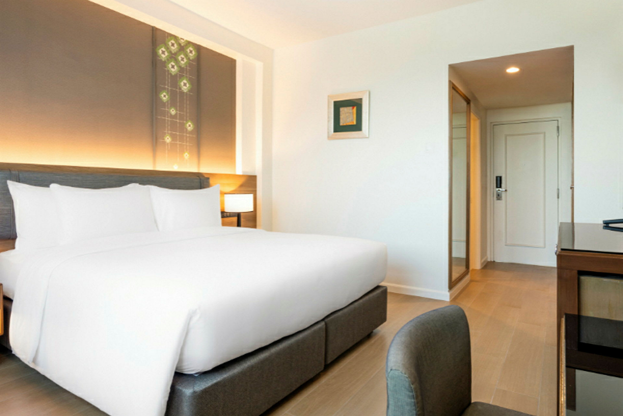 Et moderne hotellrom med en stor seng med hvite laken og sengegavl med integrert belysning. (AI-generert tekst)