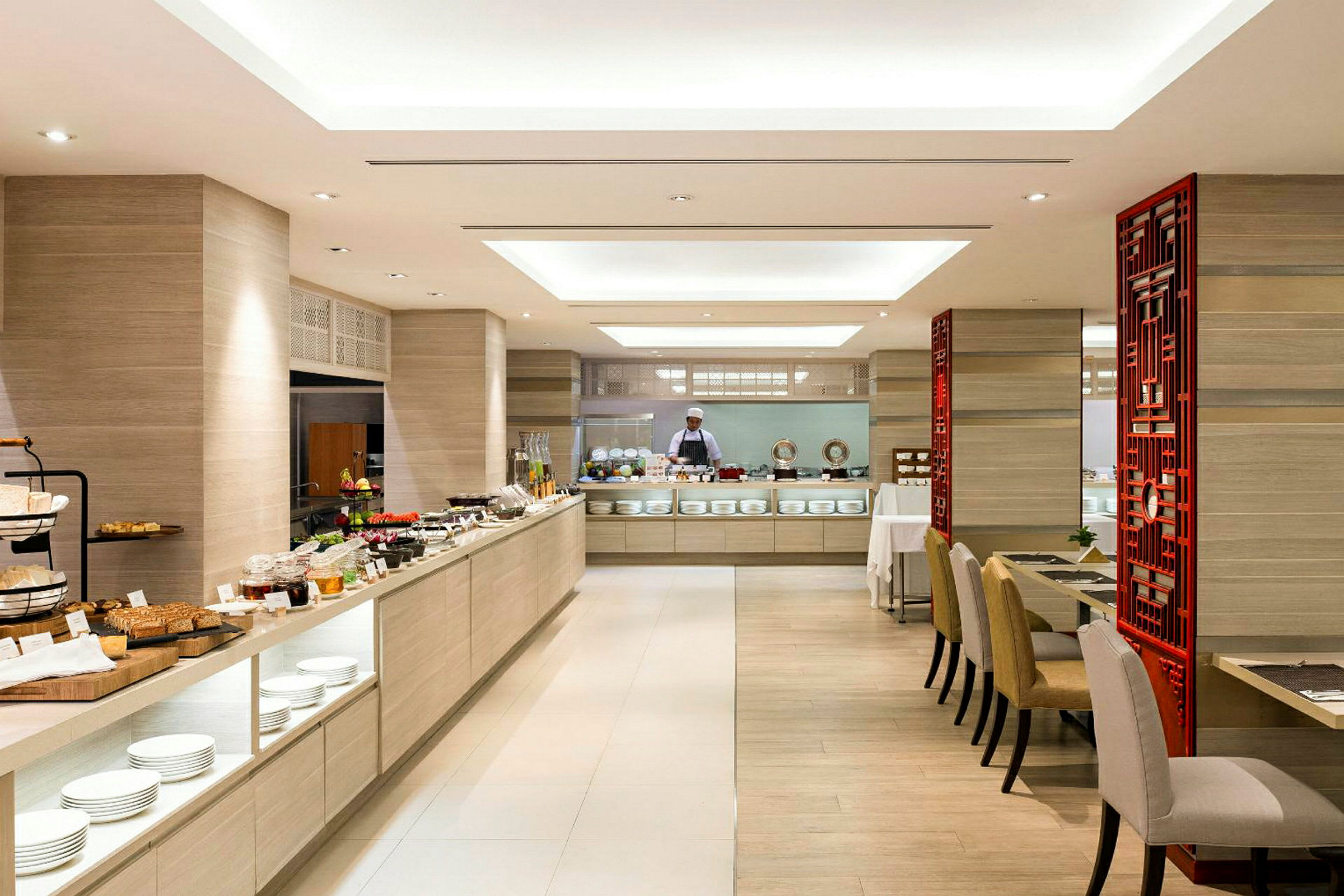 En lys restaurant med en stor buffé fullt av mat og en kokk i bakgrunnen. (AI-generert tekst)