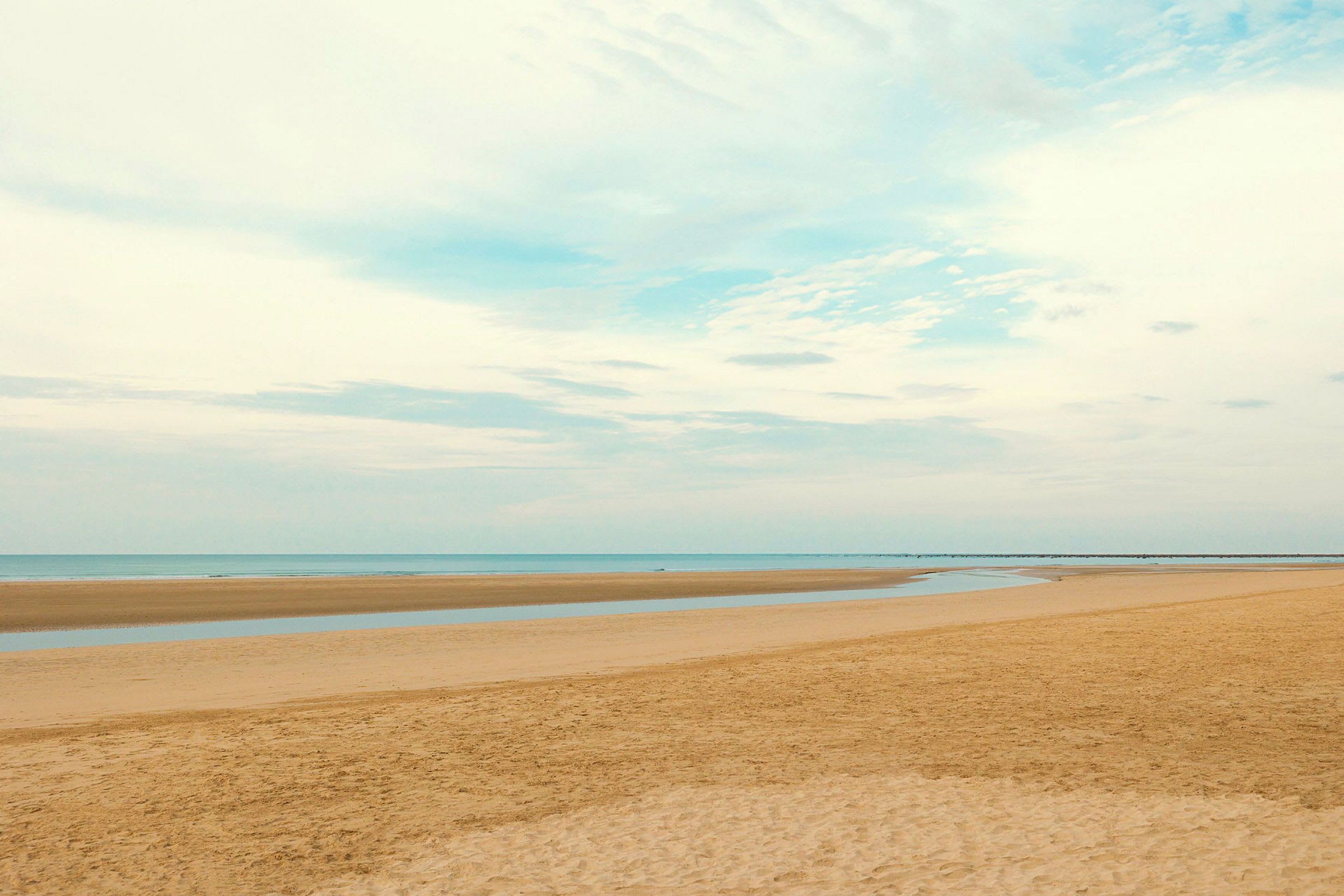 En rolig strand med utstrakt sand og havet ved horisonten. (AI-generert tekst)