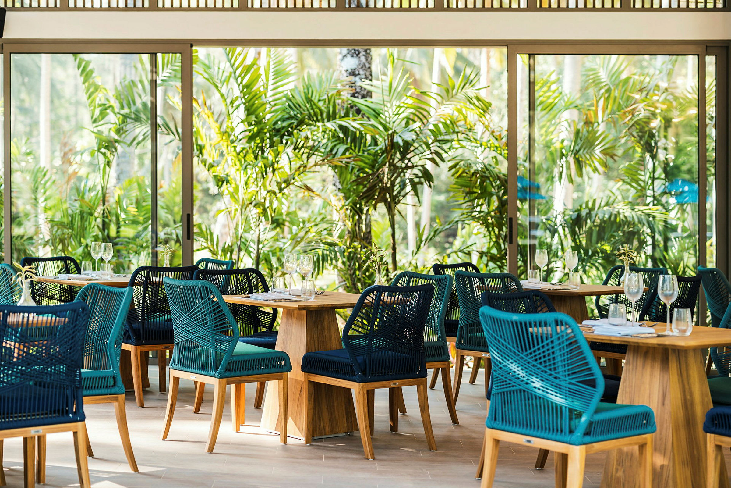 Restaurant med flettede stoler og trebord omgitt av tropisk grønt. (AI-generert tekst)
