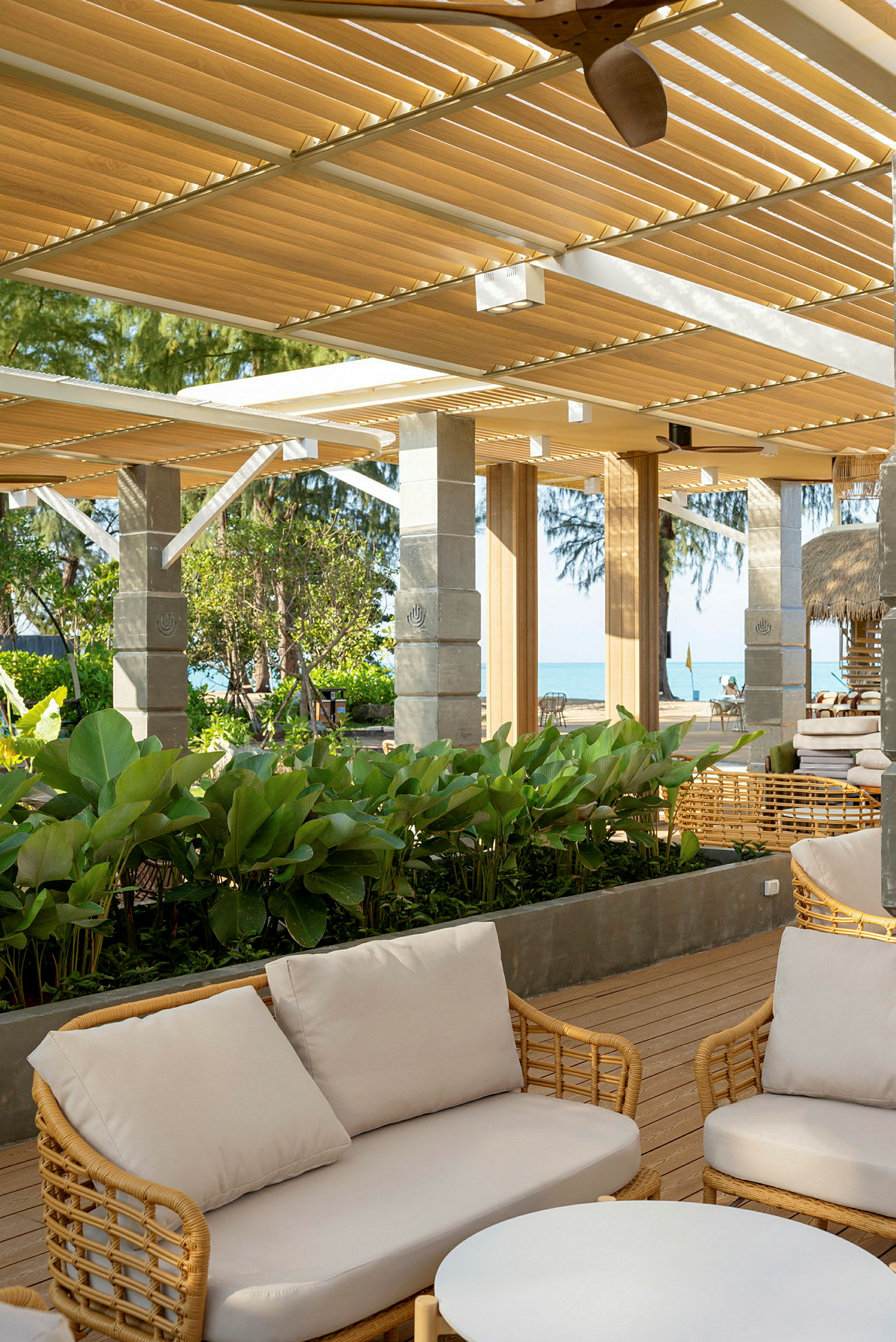 Utendørs område med sofaer og grønne planter under pergola. Havet kan sees i bakgrunnen. (AI-generert tekst)