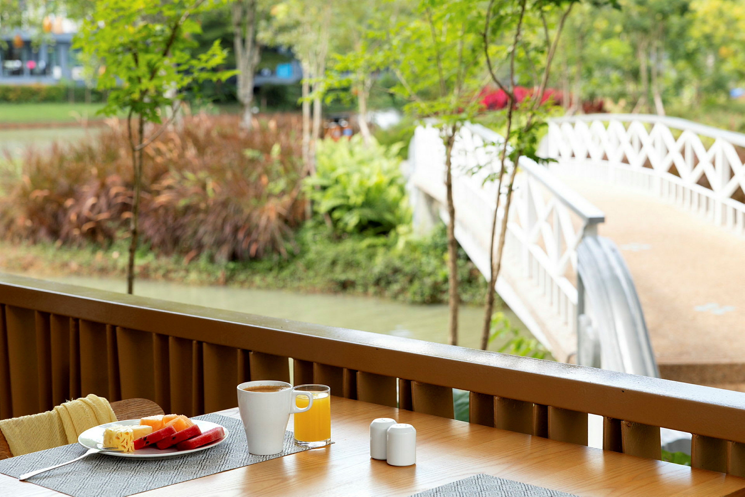 Frokostbord med kaffe og juice på en terrasse med utsikt mot en hvit bro som går over en kanal. (AI-generert tekst)