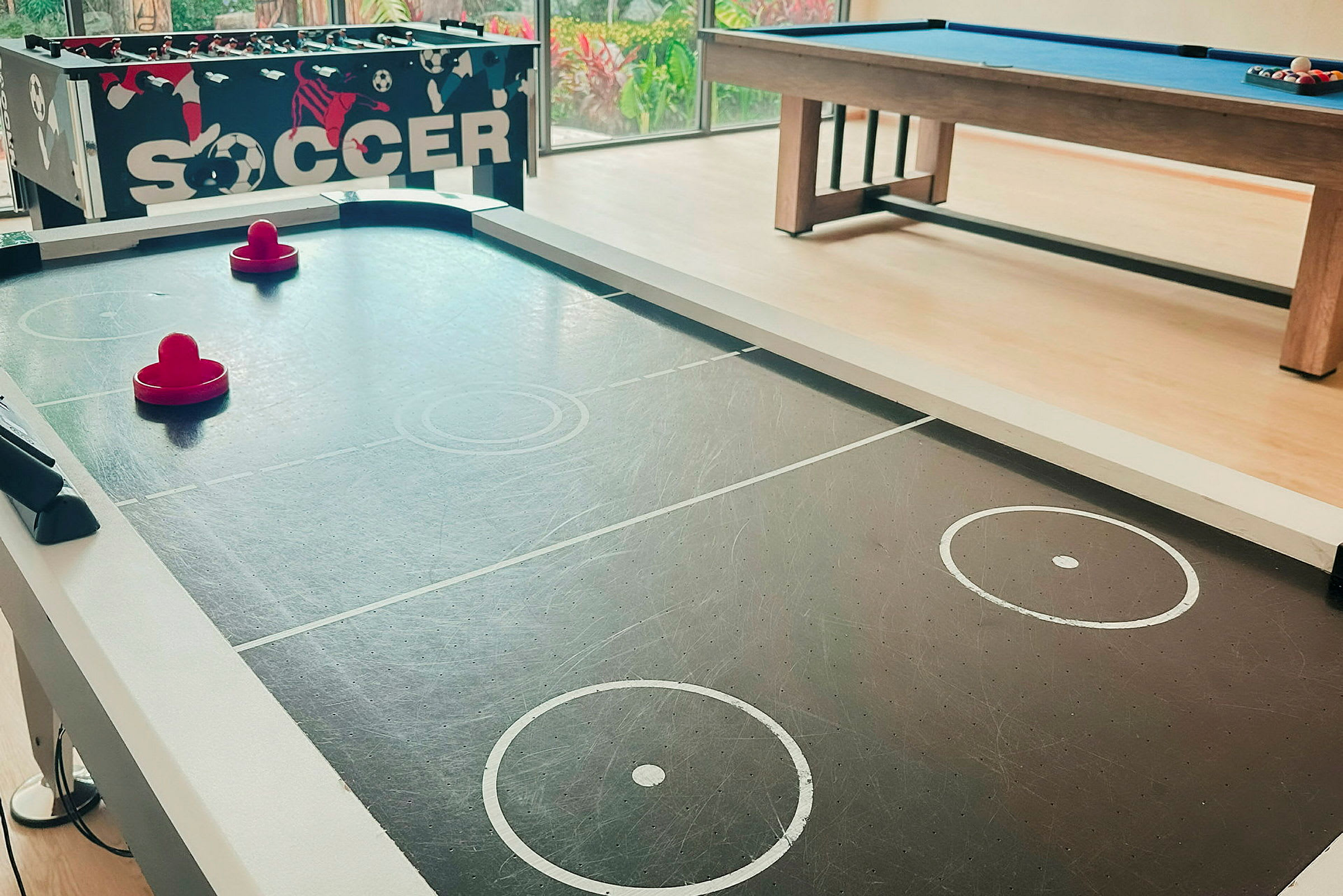 Et airhockeybord med to røde paddler og et biljardbord i bakgrunnen. (AI-generert tekst)