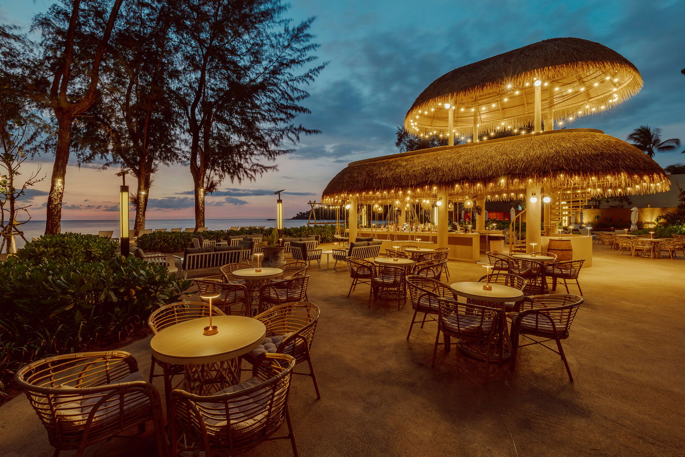 Bilde av en restaurant med stråtak og utendørs servering ved solnedgang. (AI-generert tekst)