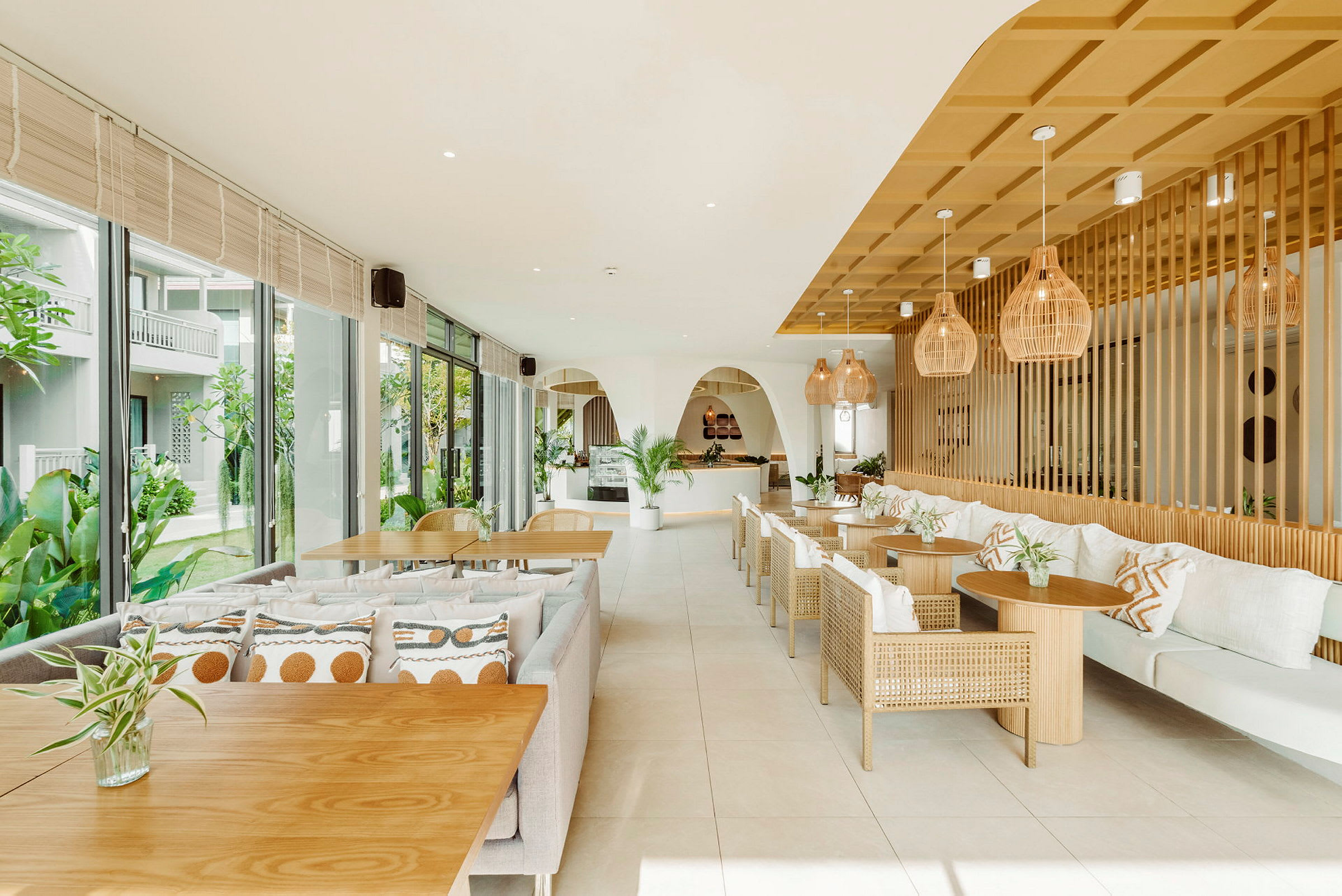 En lys og moderne restaurant med trebord og flettede stoler, dekorert med planter og innbydende puter. (AI-generert tekst)